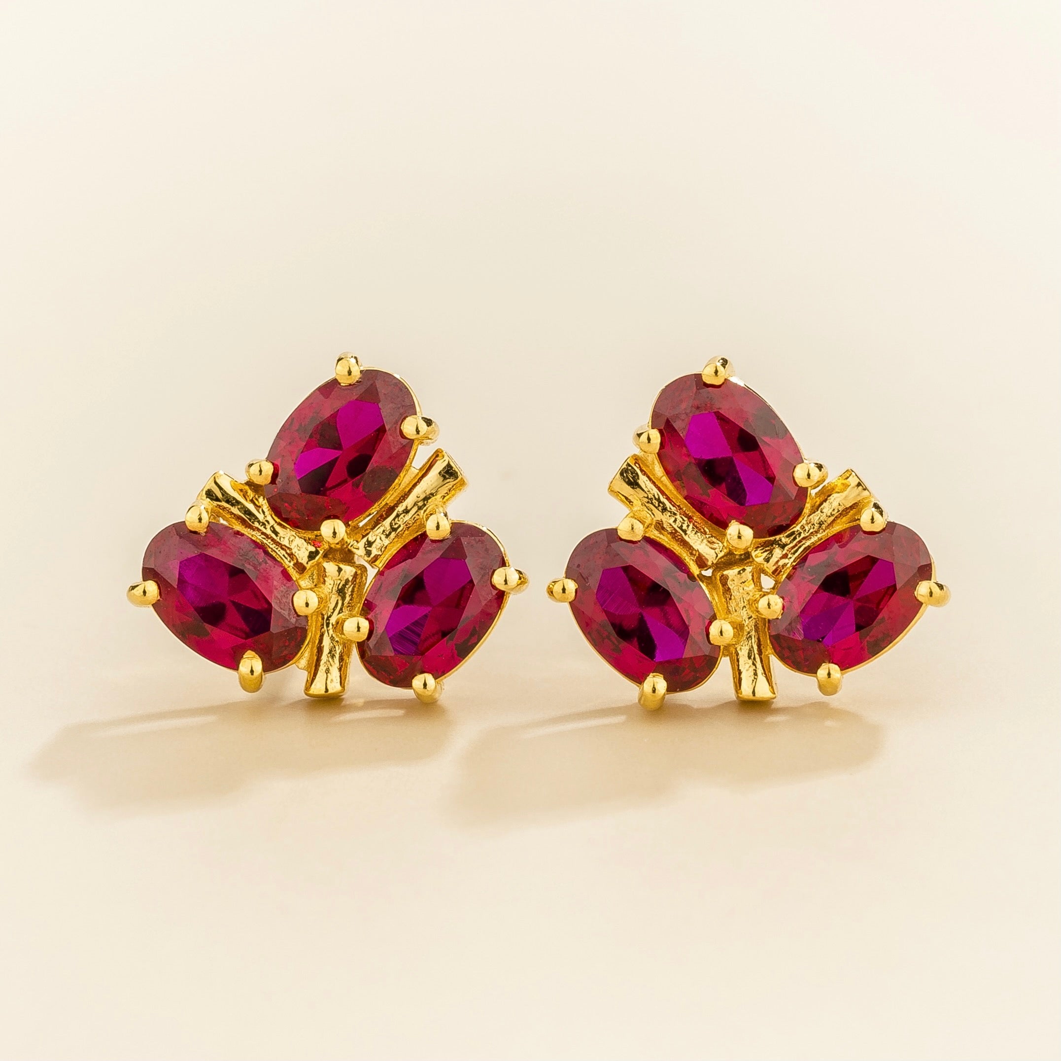 Gold earrings with 3 oval ruby cluster gemstones on a beige background