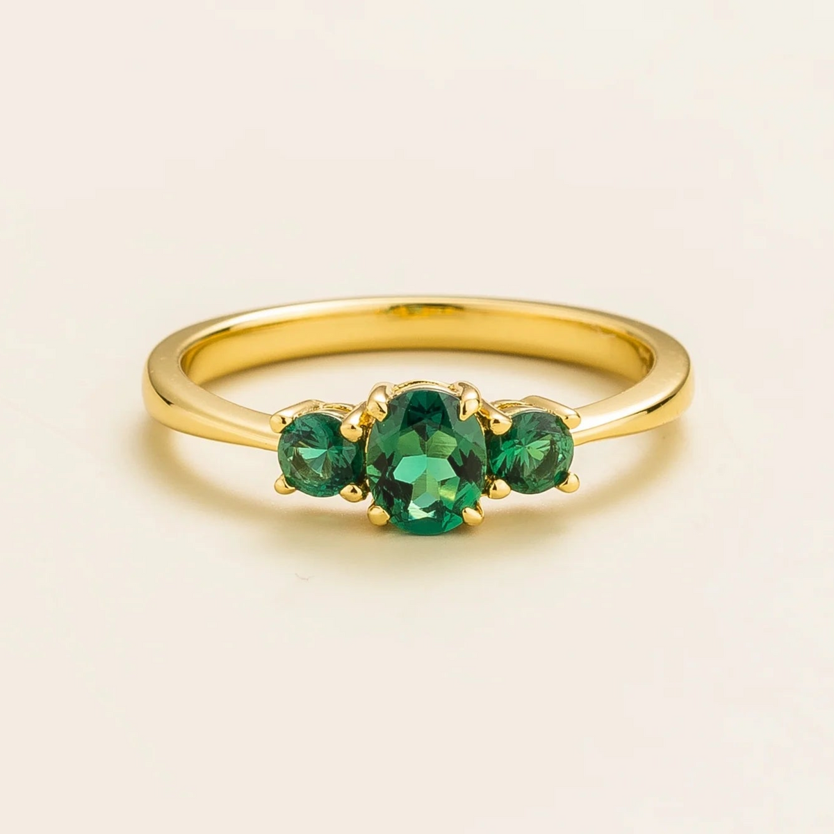 A gold ring featuring three green emerald gemstones set in a crown design.