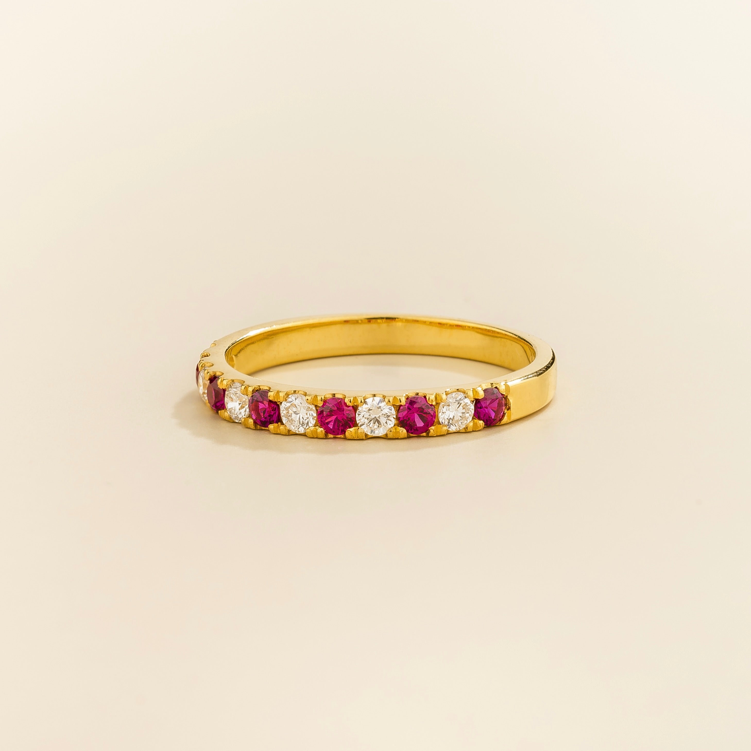 A gold ring with alternating ruby and diamond elements on a plain 