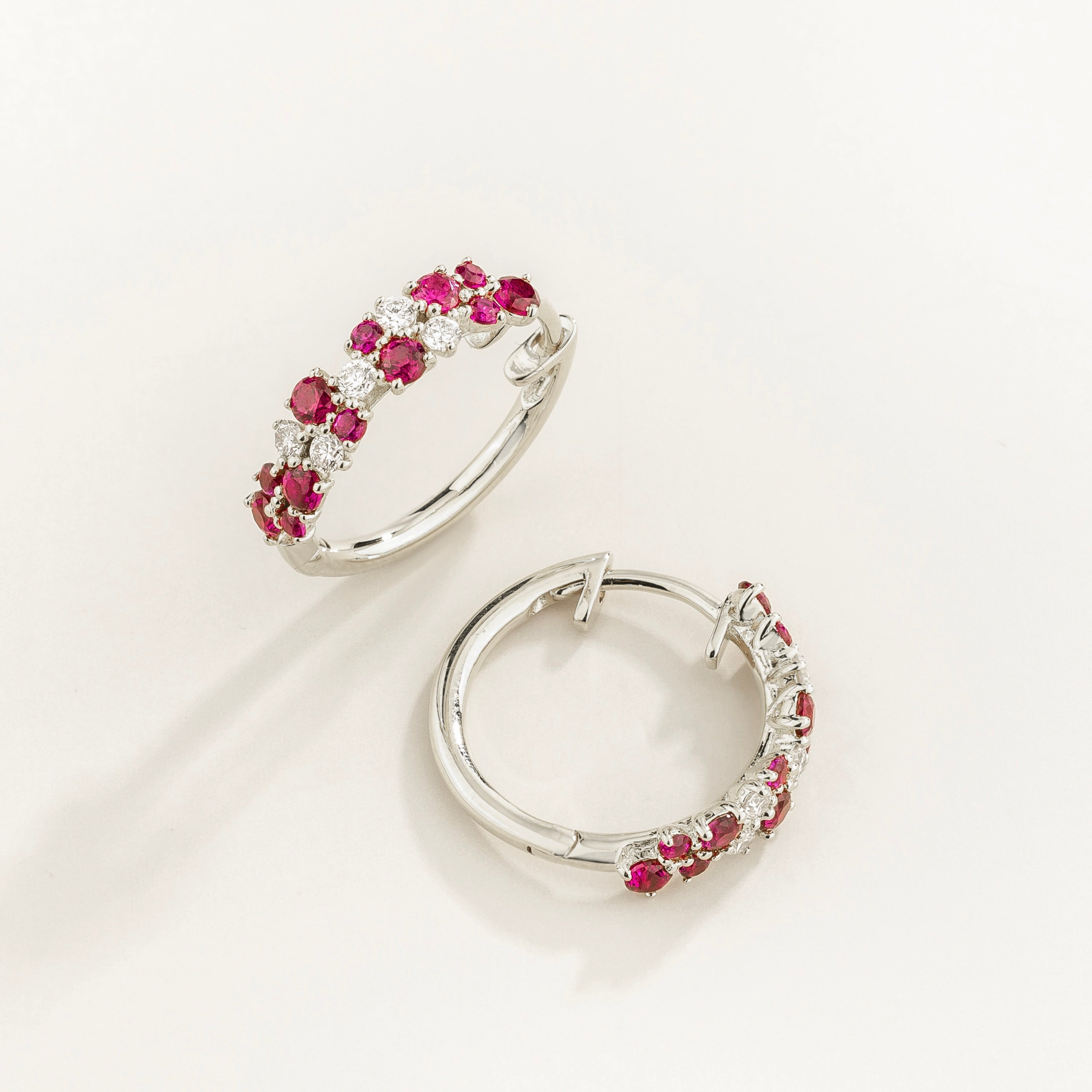 A pair of white gold huggie earrings set with cluster of round ruby and diamond accents, displayed against a neutral background.
