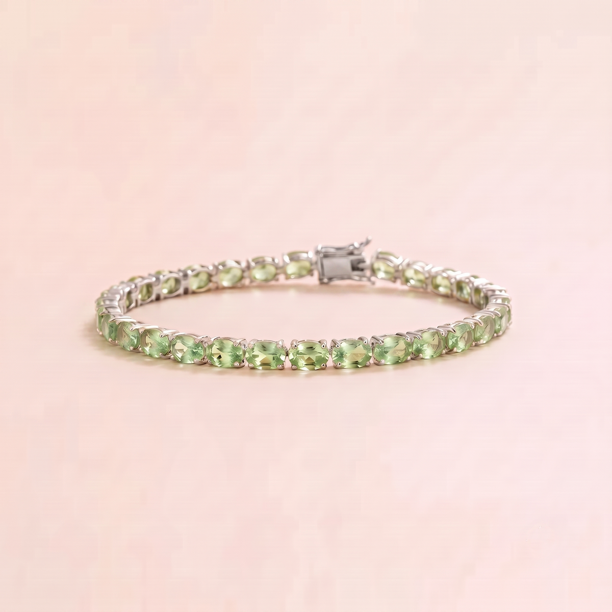 A white gold tennis bracelet set with oval green sapphire gemstones.