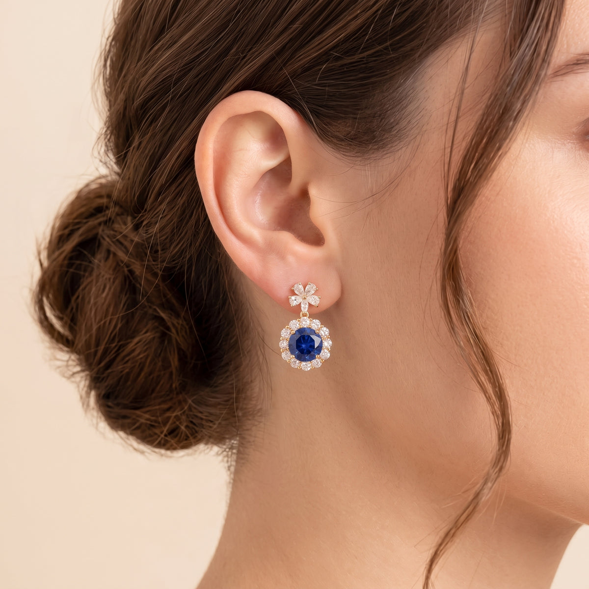 A model is wearing The Antoinette Round Blue Sapphire & Diamond Halo Pendant Earrings with Flower Bail