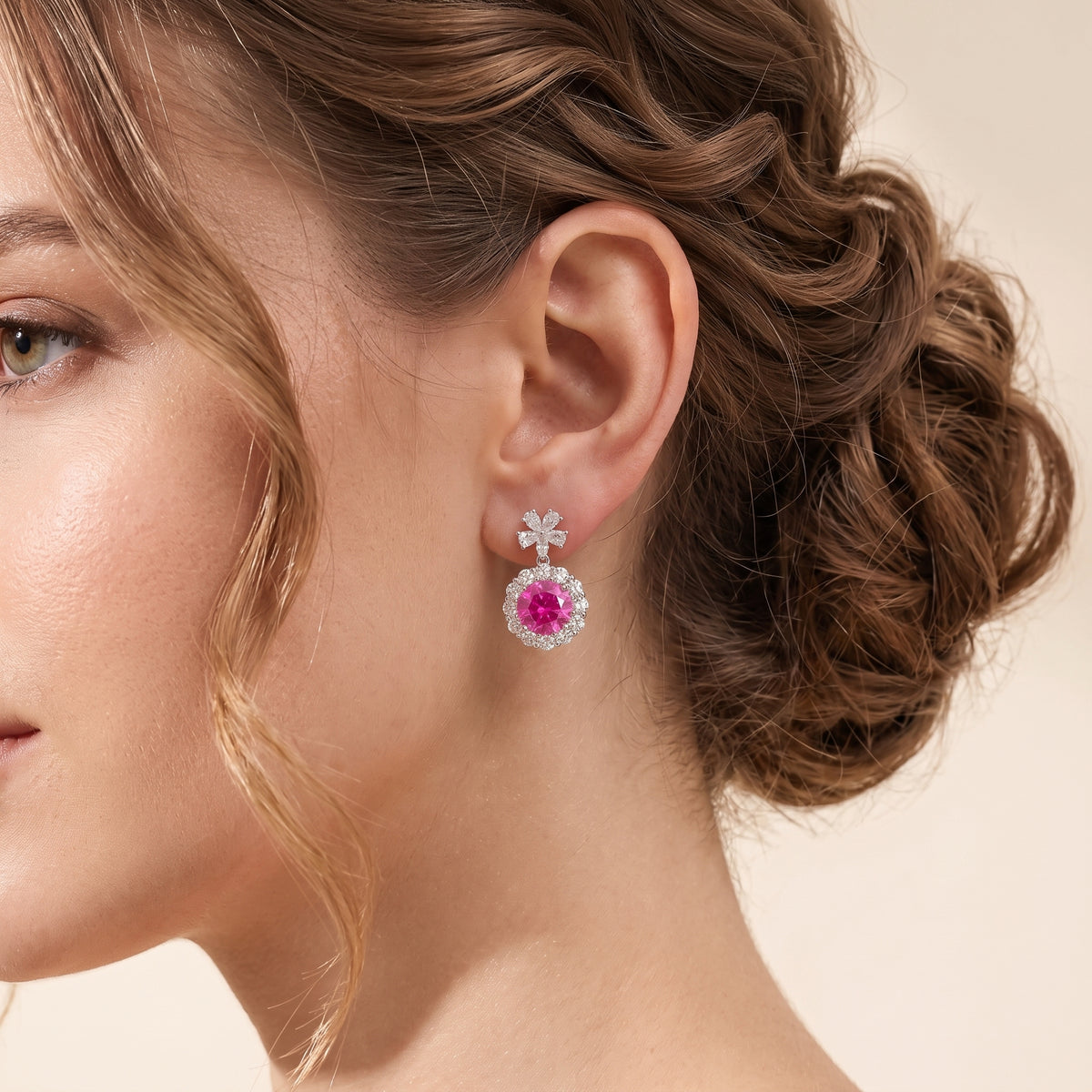 A model is wearing The Antoinette Round Vivid Pink Sapphire & Diamond Halo Pendant Earrings with Flower Bail