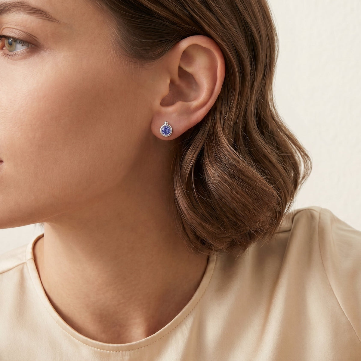A model is wearing Kiki Blue Sapphire Round Bezel Set Solitaire Earrings in White Gold