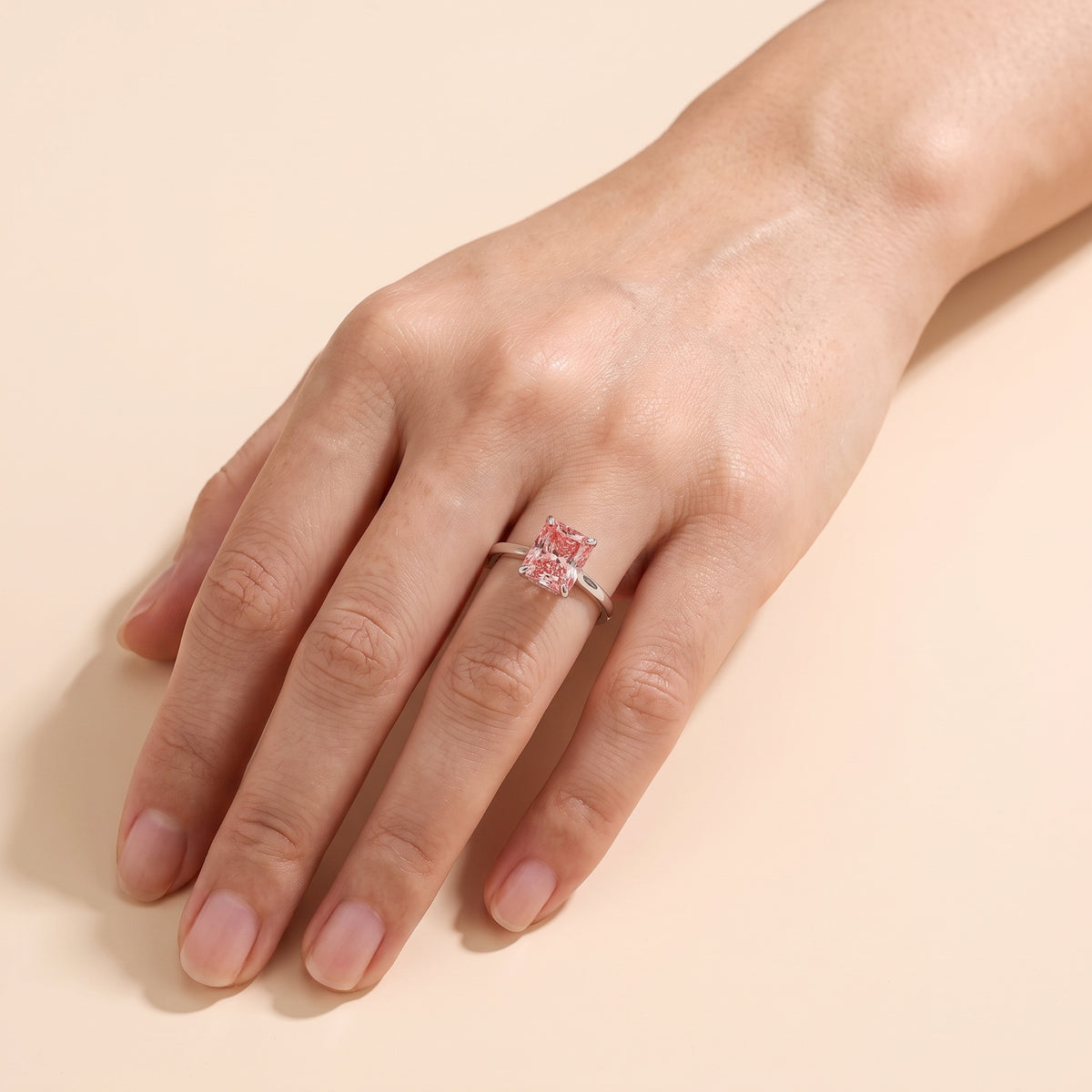 A model is wearing The Clair Radiant Shape Padparadscha Sapphire Cathedral Solitaire 