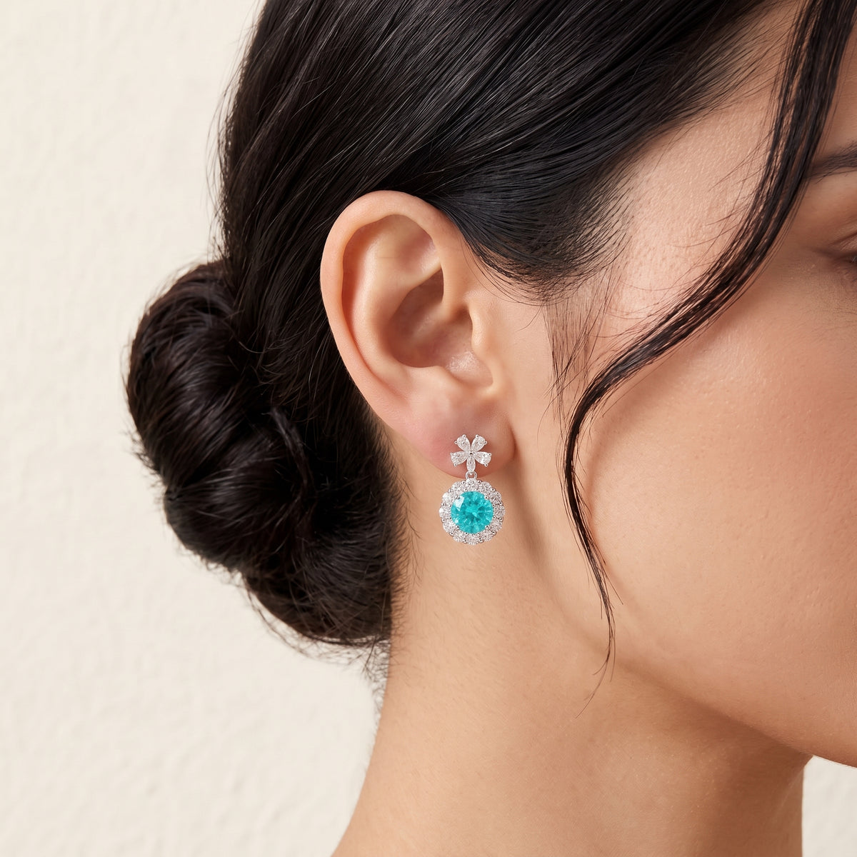 A model is wearing The Antoinette Round Paraiba Tourmaline & Diamond Halo Pendant Earrings with Flower Bail