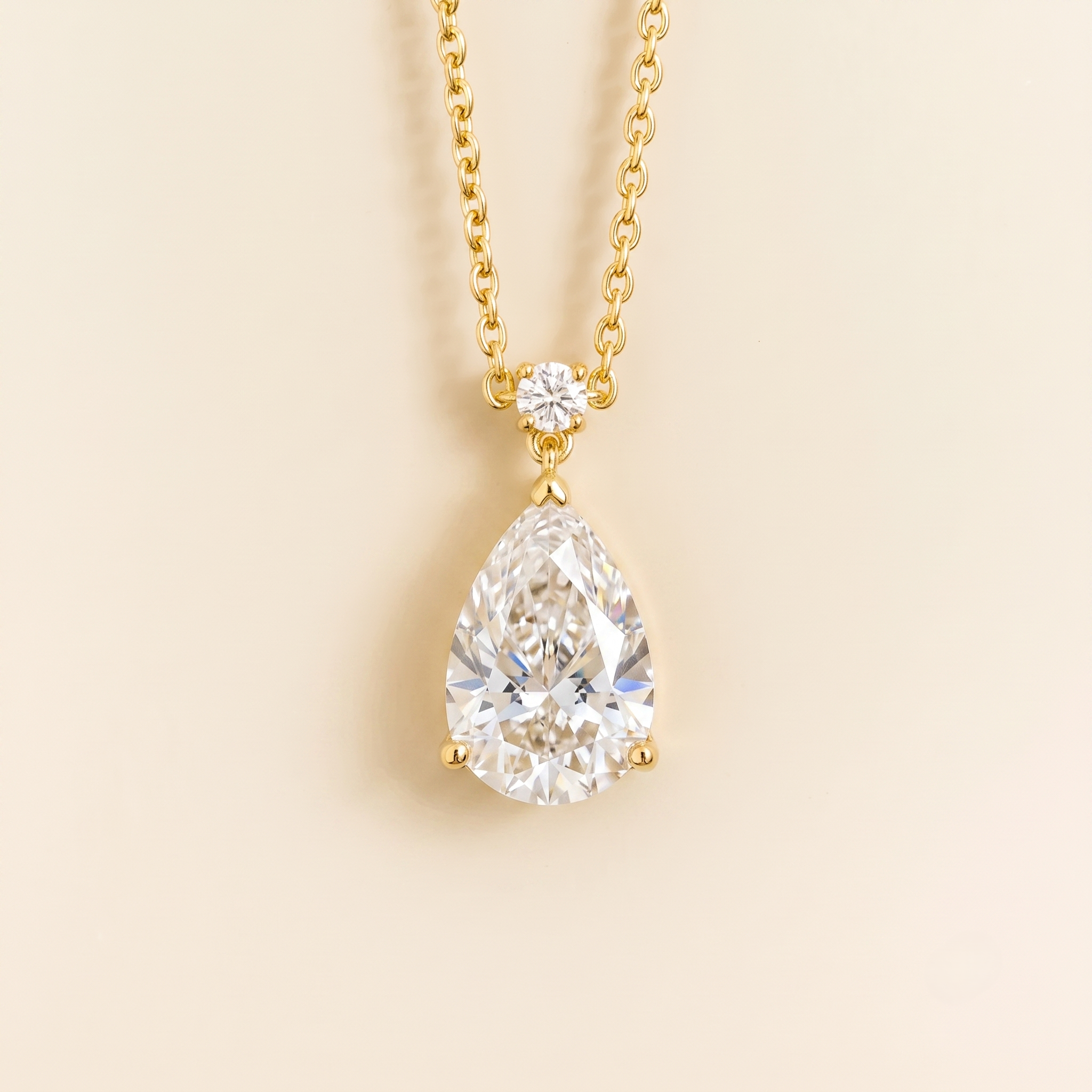 Classic gold necklace with a teardrop pear shape diamond pendant with a smaller round diamond accent, on a beige background