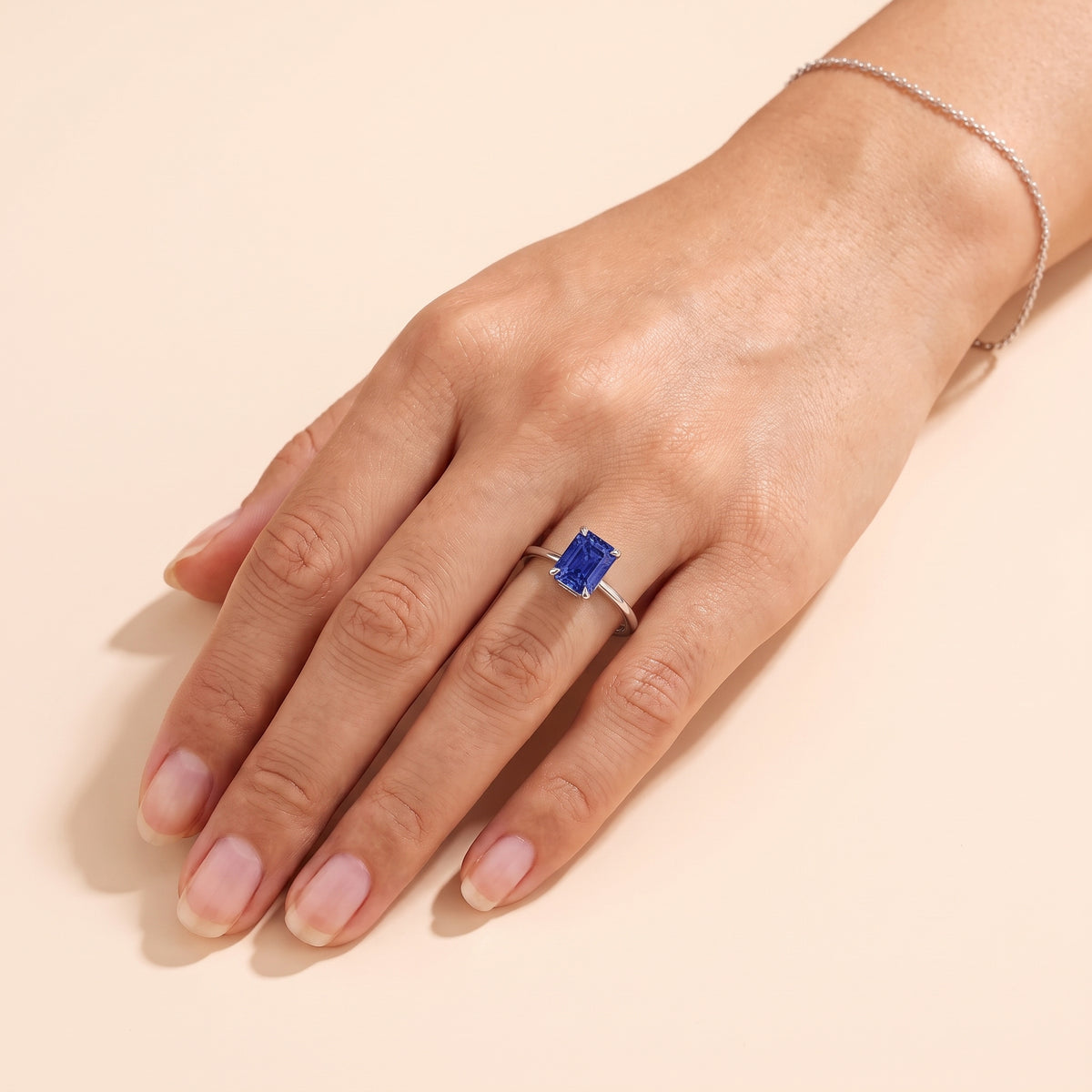 A model is wearing The Clair Radiant Shape Blue Sapphire Cathedral Solitaire Ring