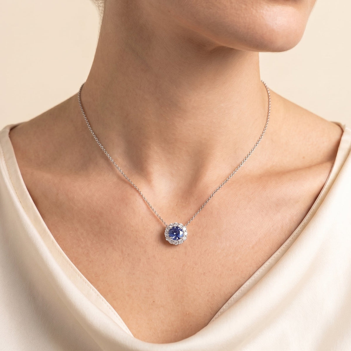 A model is wearing Zoe Blue Sapphire Round & Diamond Halo Necklace In White Gold
