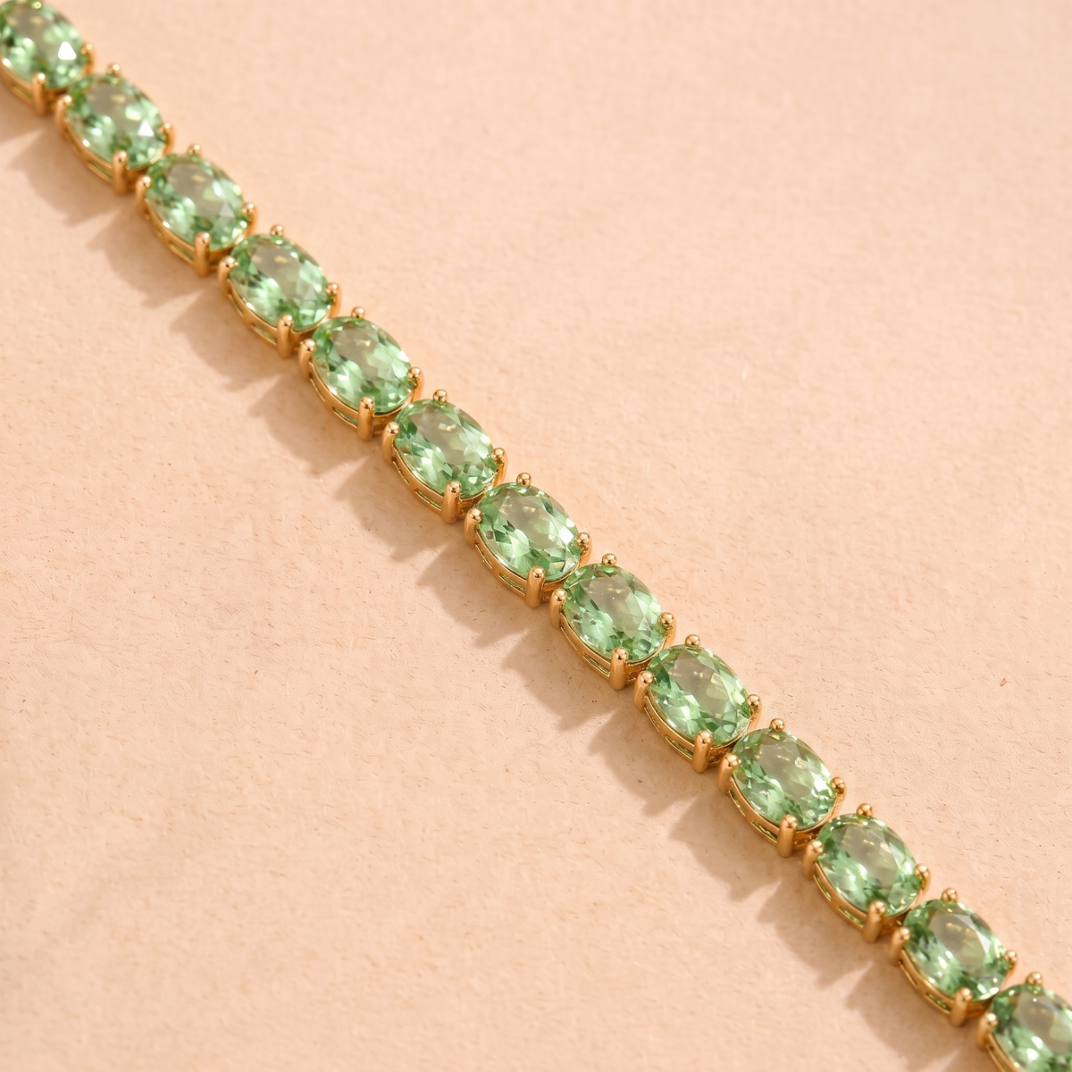 A gold tennis bracelet set with oval green sapphire gemstones.