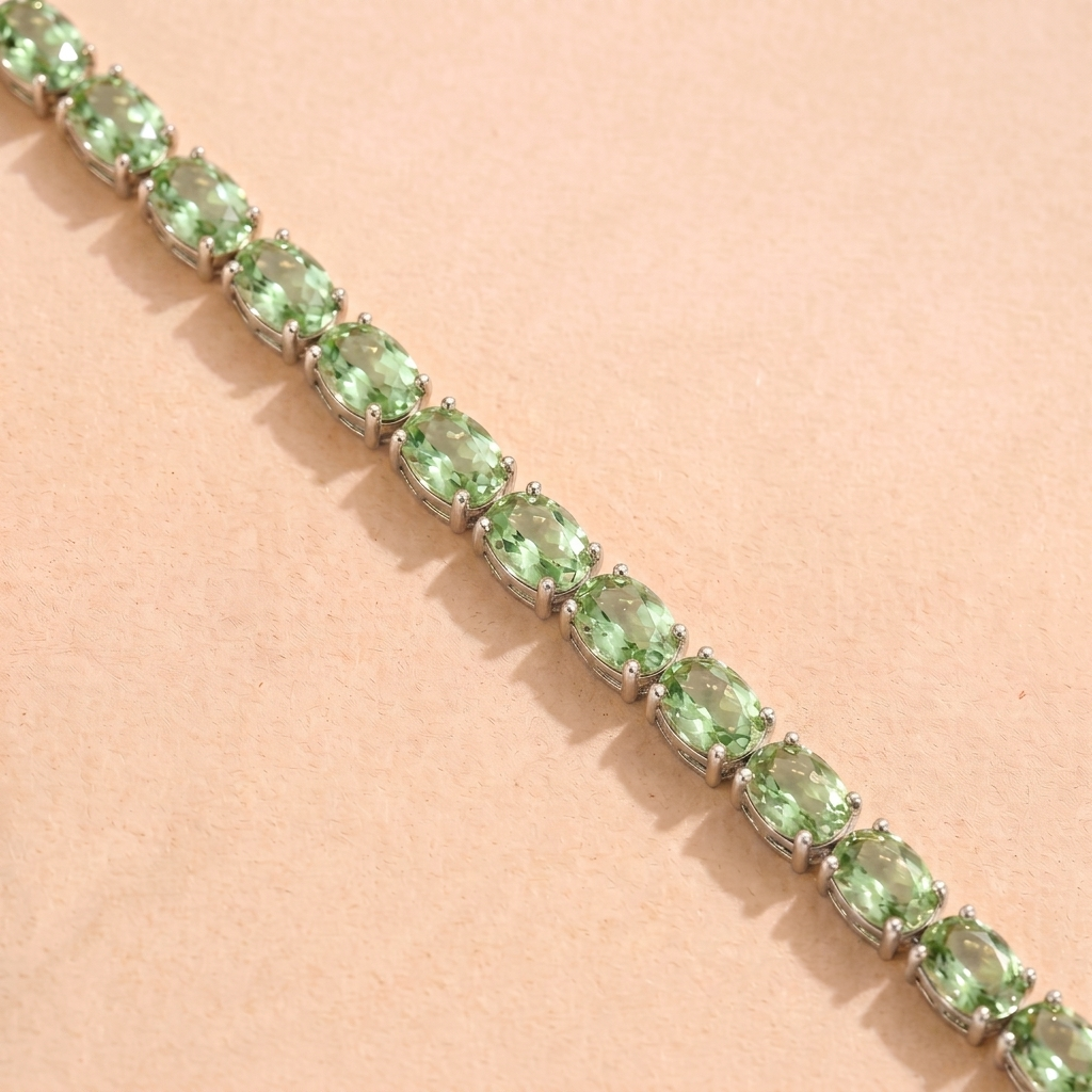 A white gold tennis bracelet set with oval green sapphire gemstones.