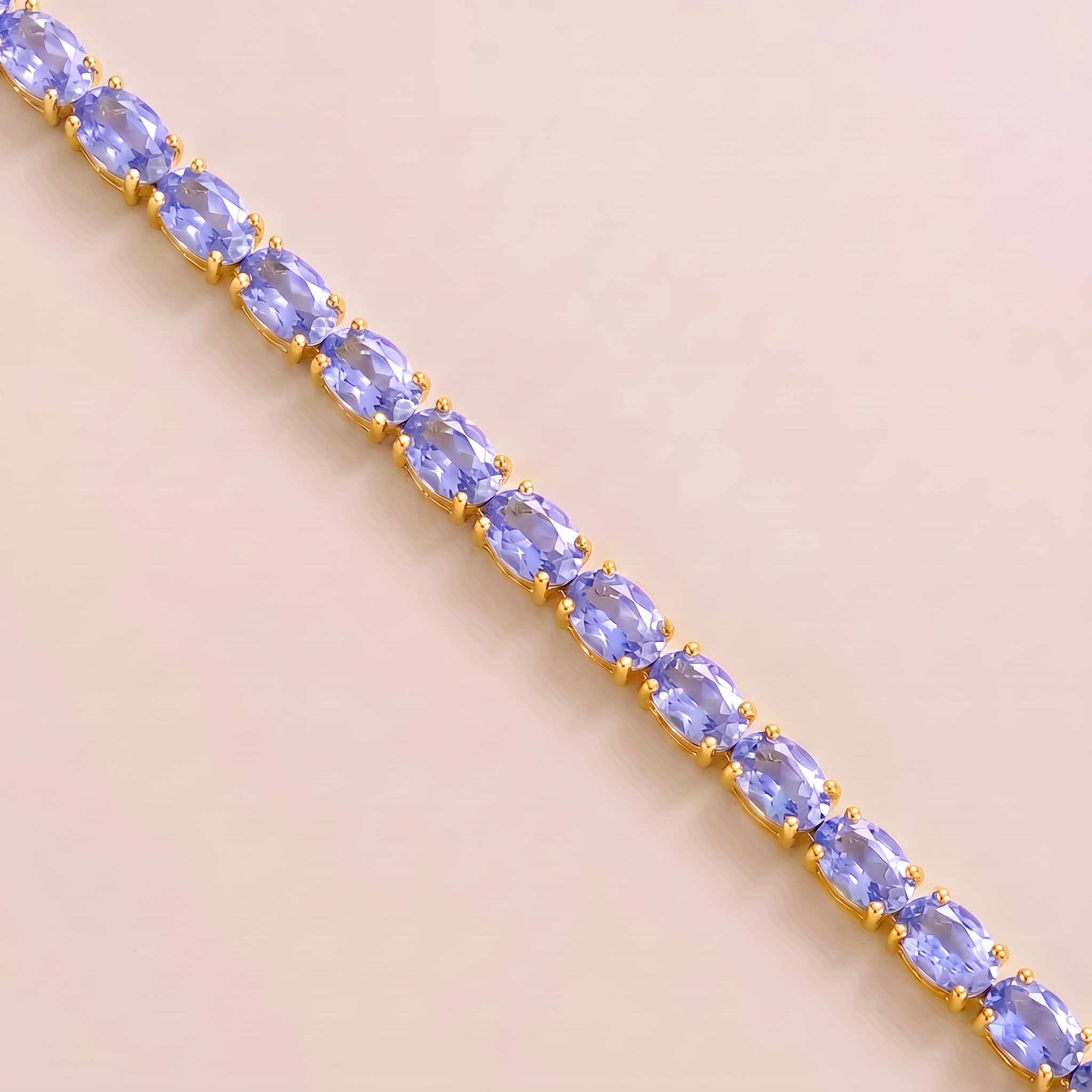 A gold tennis bracelet set with oval light blue sapphire gemstones.