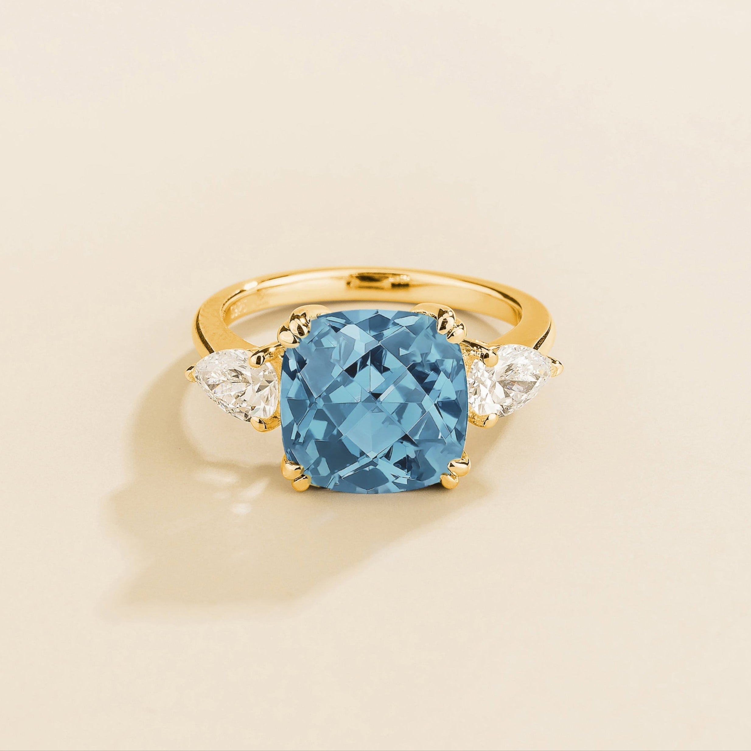 Gold ring with cushion cut aquamarine gemstone and pear side diamonds on a beige background