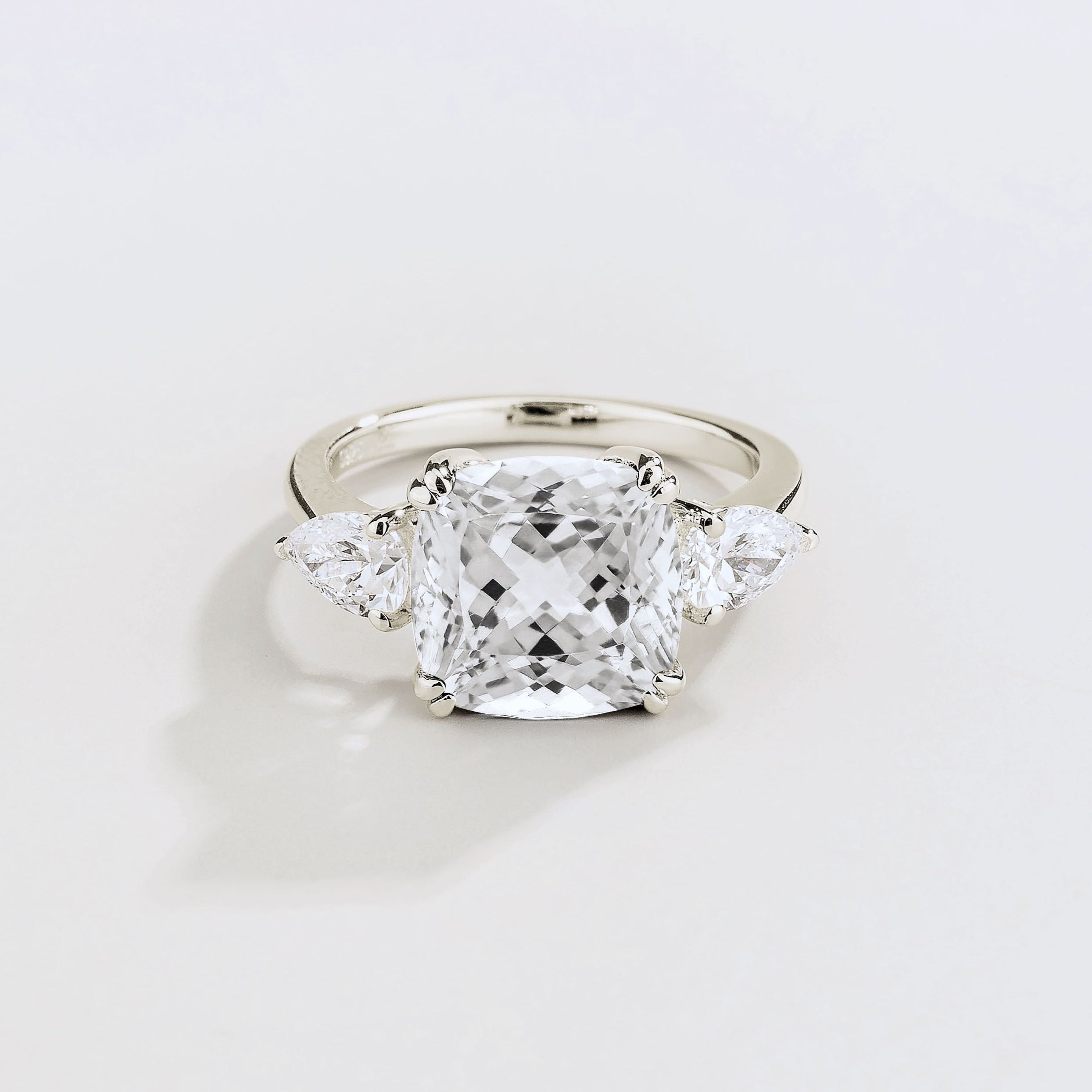 White gold ring with large cushion cut diamond gemstone and pear side diamonds on a beige background