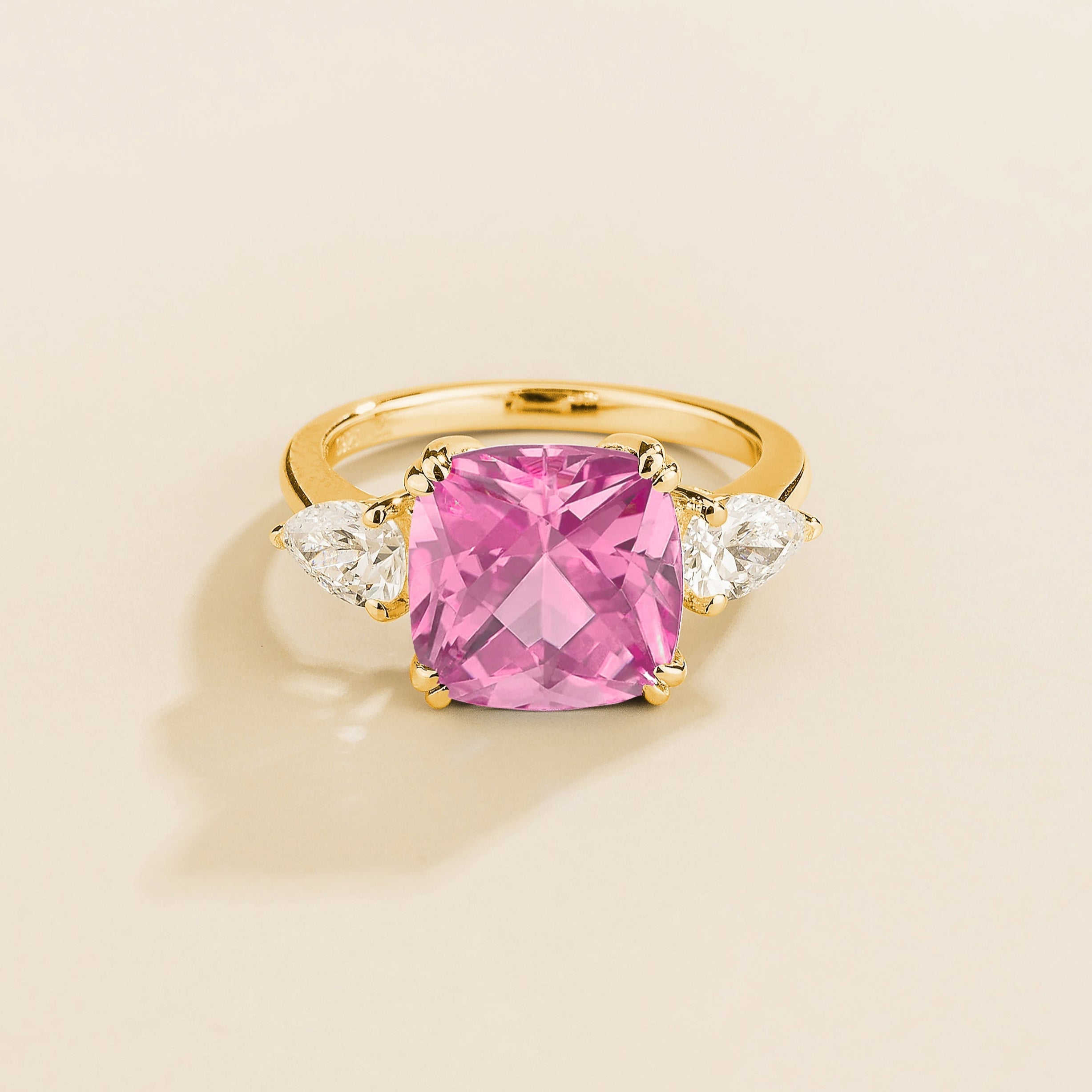 A gold ring with a large pink cushion-cut sapphire centerpiece and smaller pear-cut diamond accents on the sides.