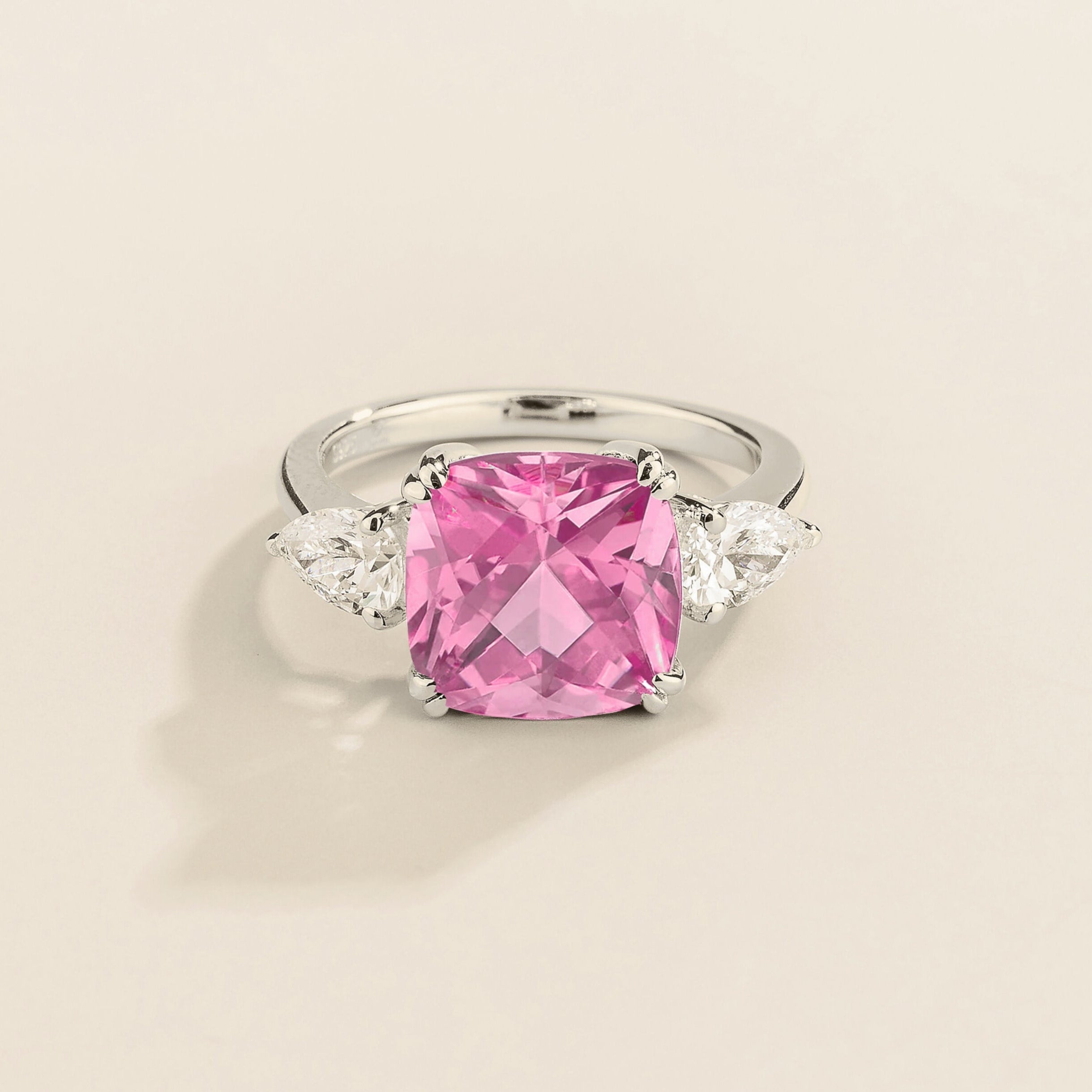A white gold ring with a large pink cushion-cut sapphire centerpiece and smaller pear-cut diamond accents on the sides.