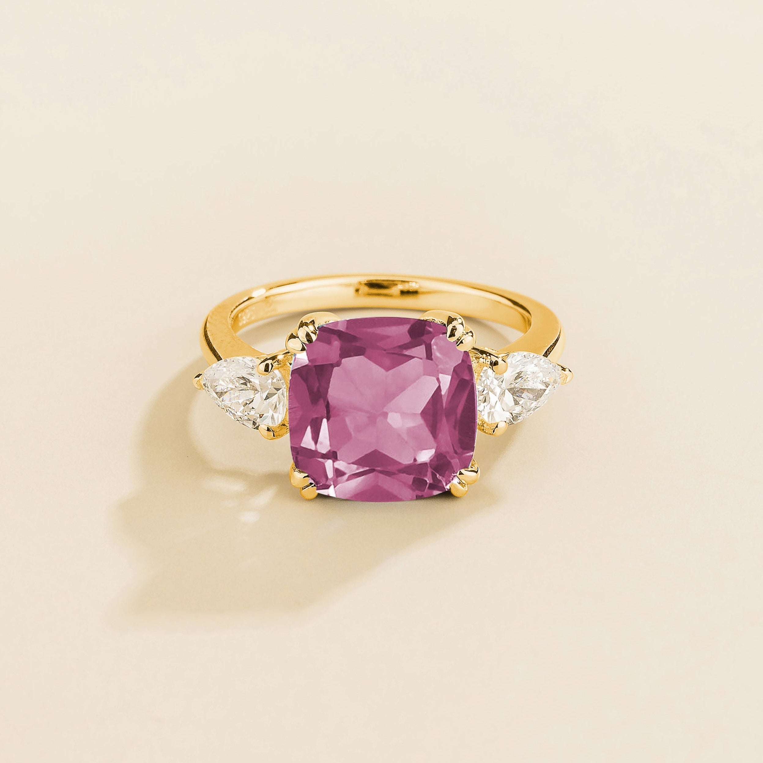 Gold ring with cushion cut morganite gemstone and pear side diamonds on a beige background