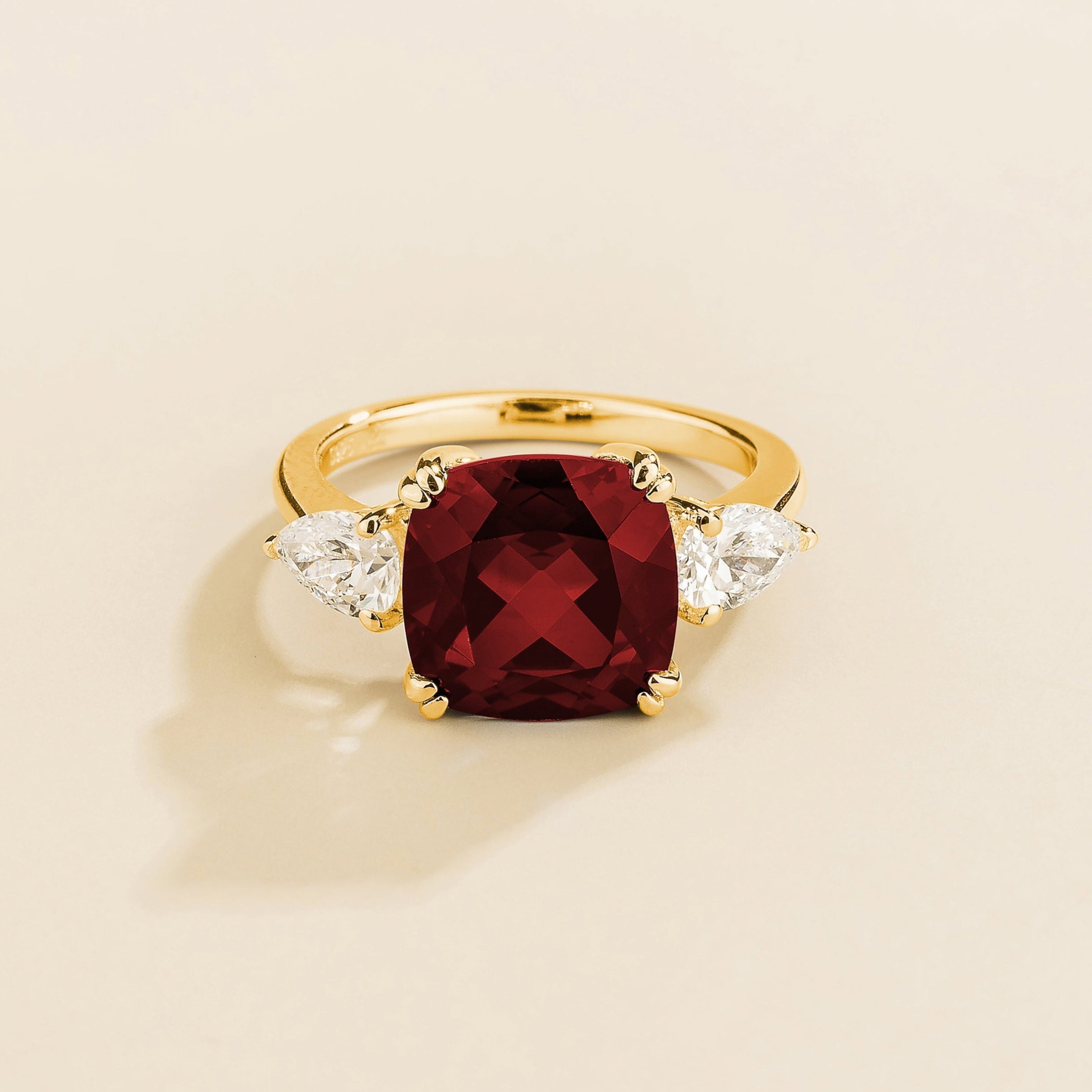 Gold ring with cushion cut ruby gemstone and pear side diamonds on a beige background