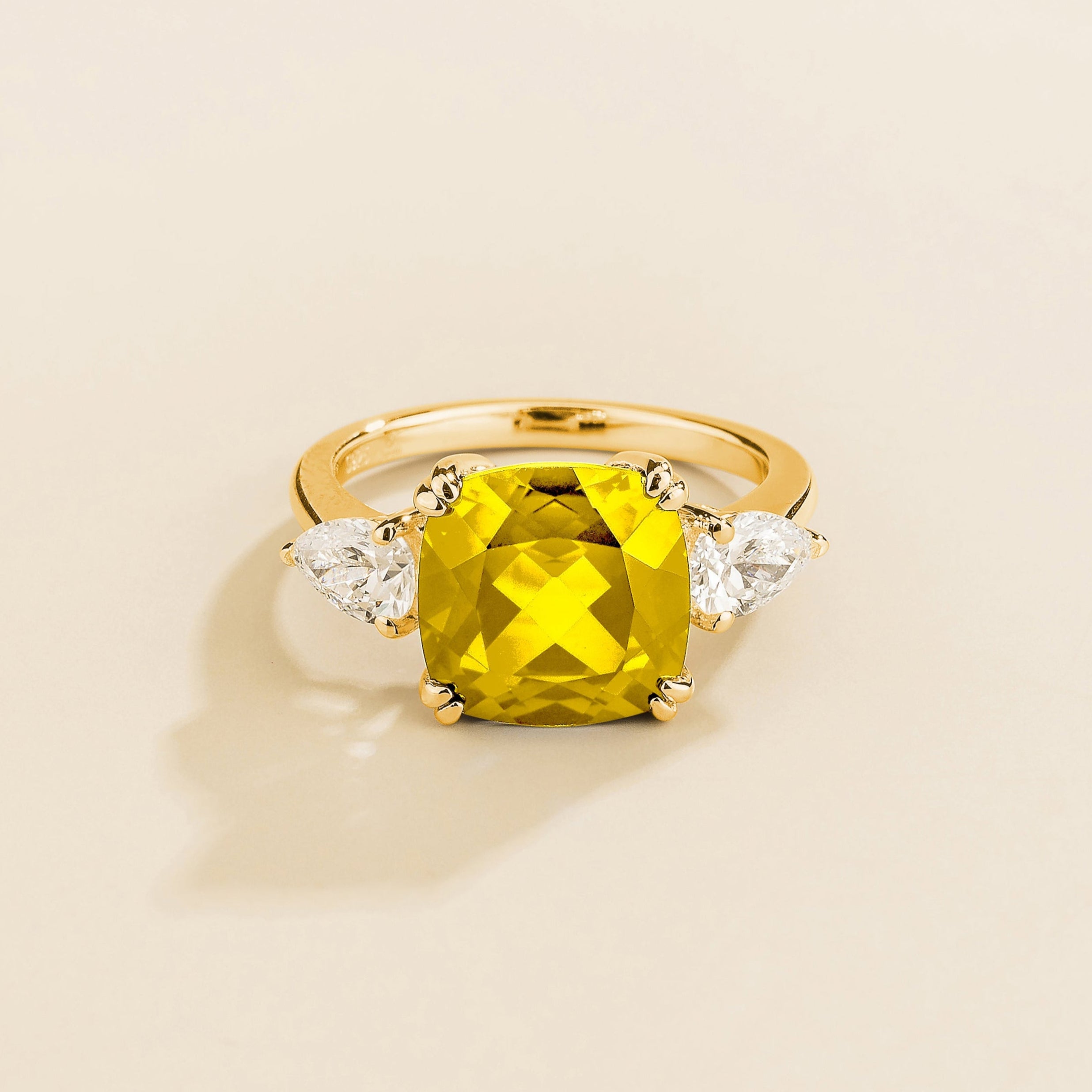 Gold ring with cushion cut yellow sapphire gemstone and pear side diamonds on a beige background