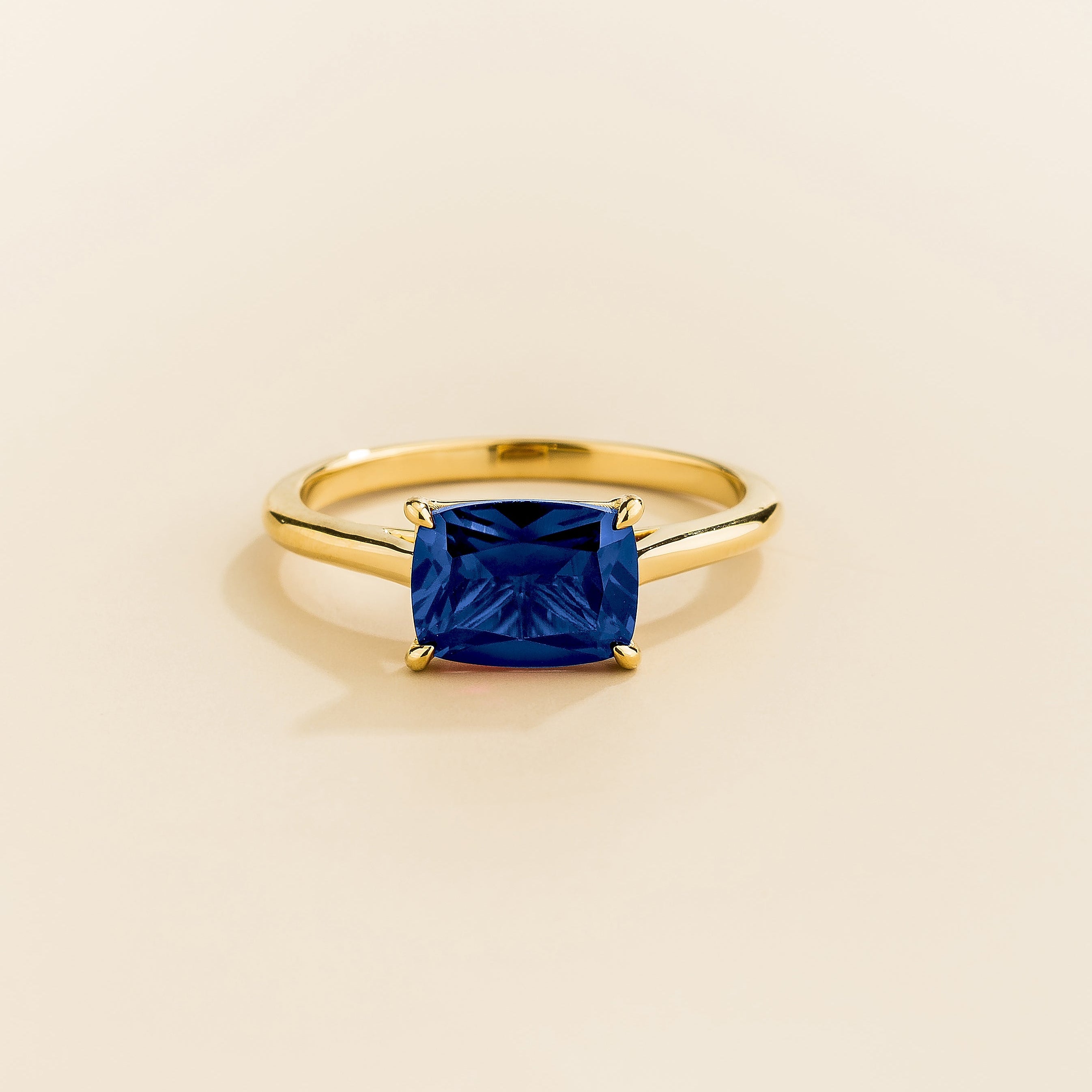 Juvetti yellow gold ring featuring a cushion-cut lab-grown blue sapphire in an east–west setting.