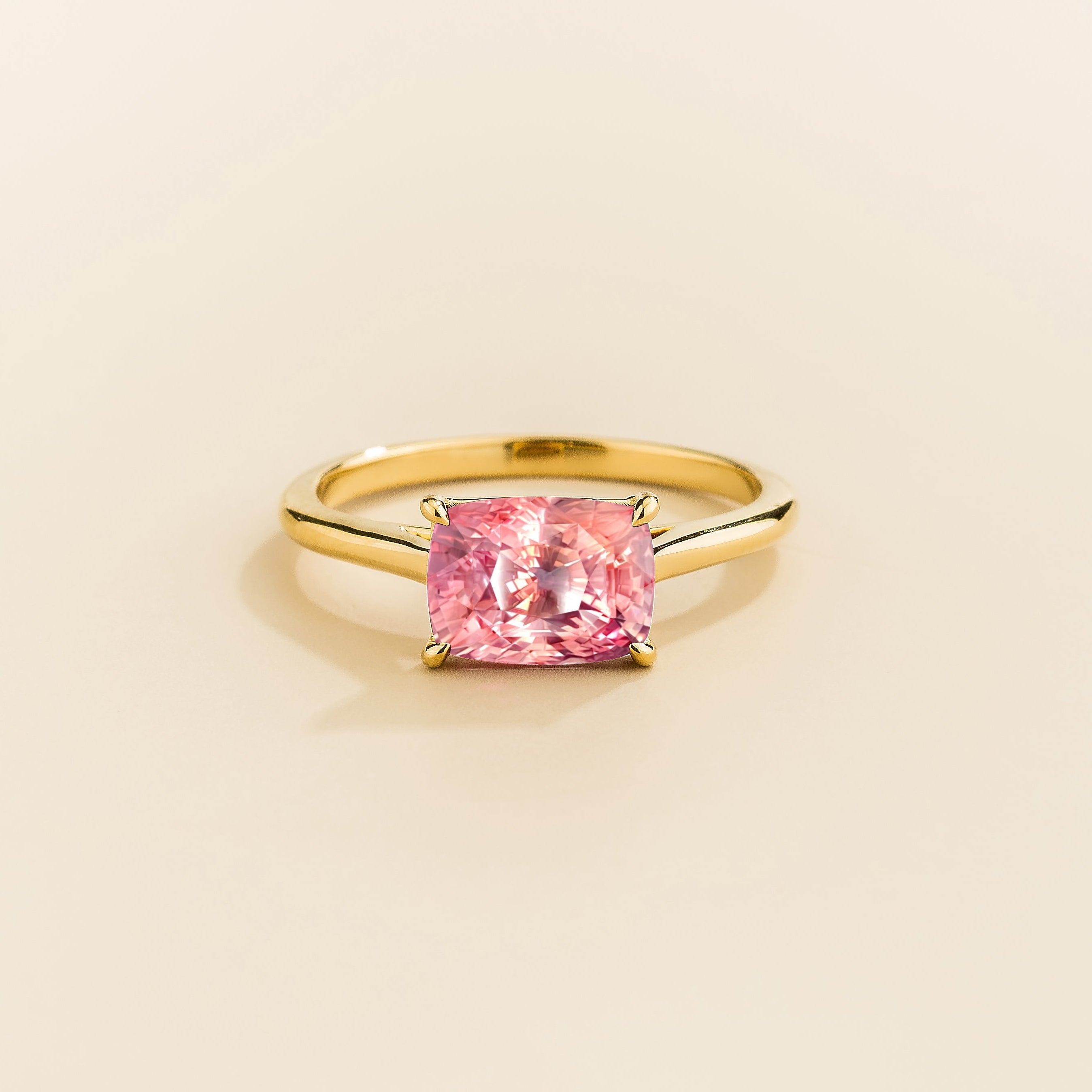Kissen Ring in gold, set with a Padparadscha Sapphire in an east–west setting.