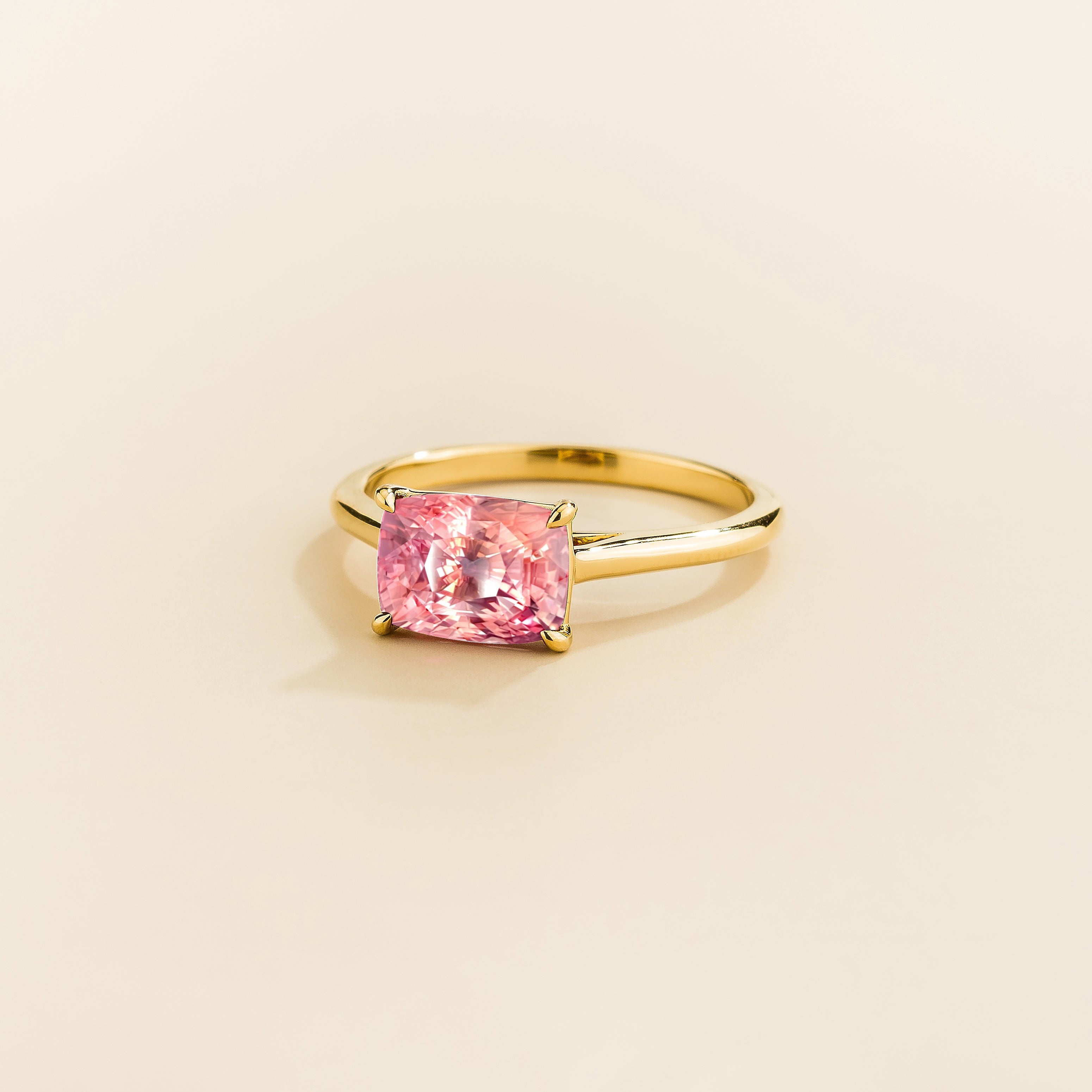 Kissen Ring in gold, set with a Padparadscha Sapphire in an east–west setting.