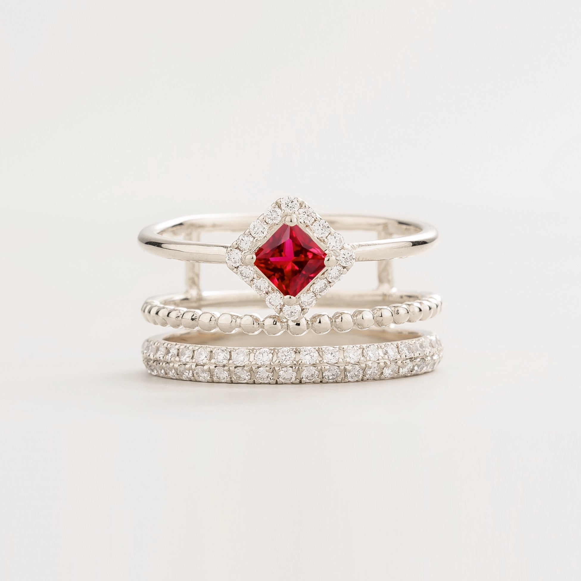 Stack of three silver rings with a red ruby gemstone in process cut and round diamonds pavé