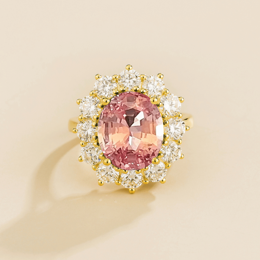 Juvetti yellow gold halo ring featuring an oval lab-grown padparadscha sapphire surrounded by round lab-grown diamonds.