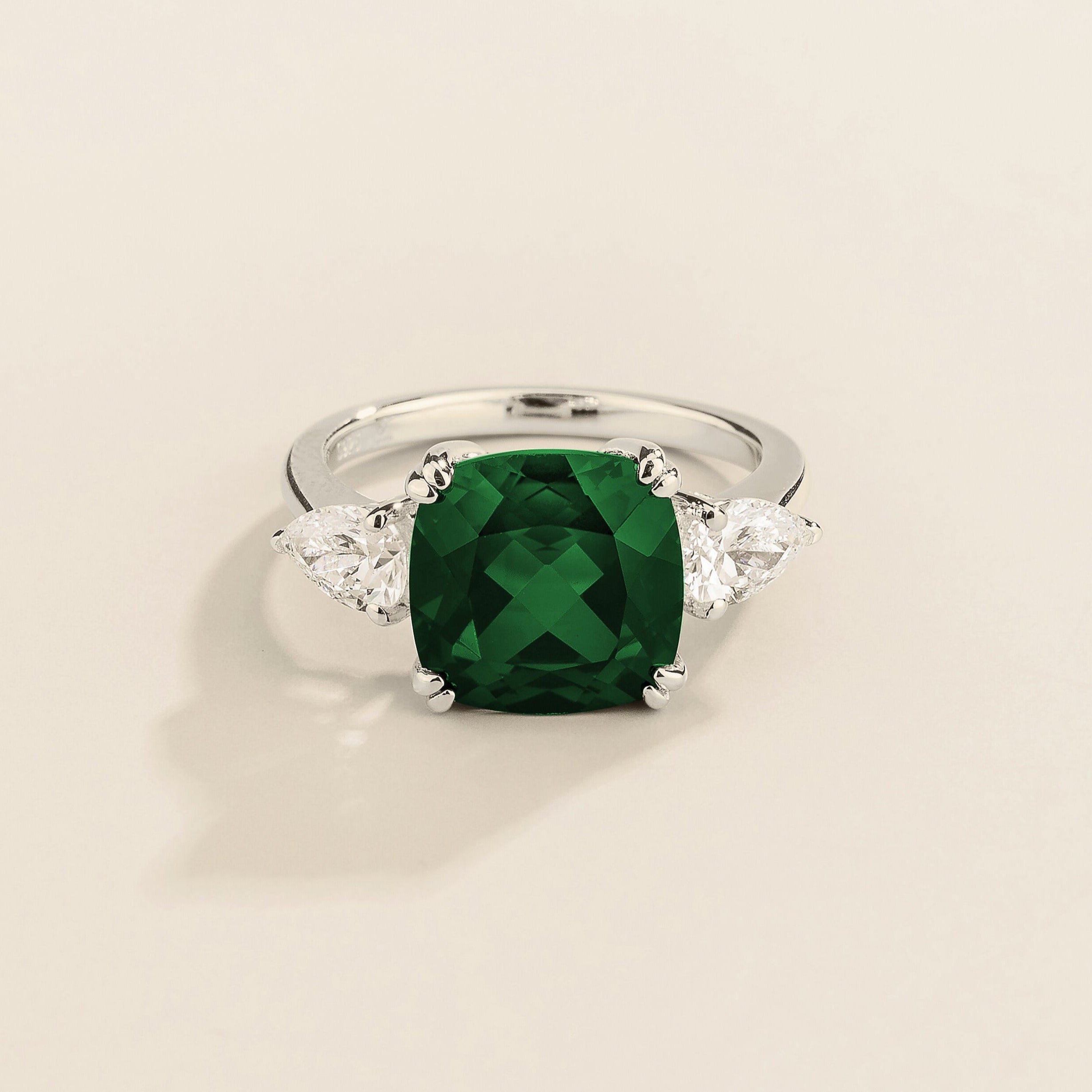 A white gold ring with a large emerald cushion-cut centerpiece and smaller pear-cut diamond accents on the sides.
