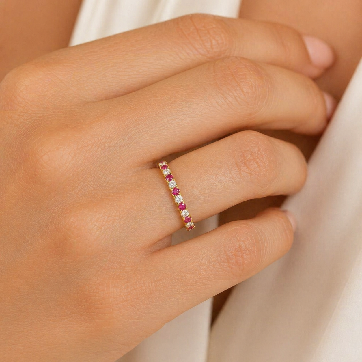Close-up of a hand wearing a ring with daiamond and ruby gemstones on a neutral background
