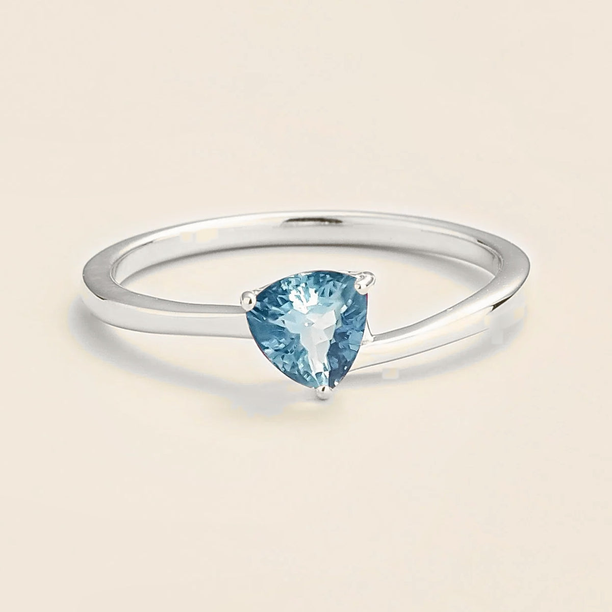 A solitaire white gold ring featuring a trillion-cut aquamarine in a unique modern curved setting.