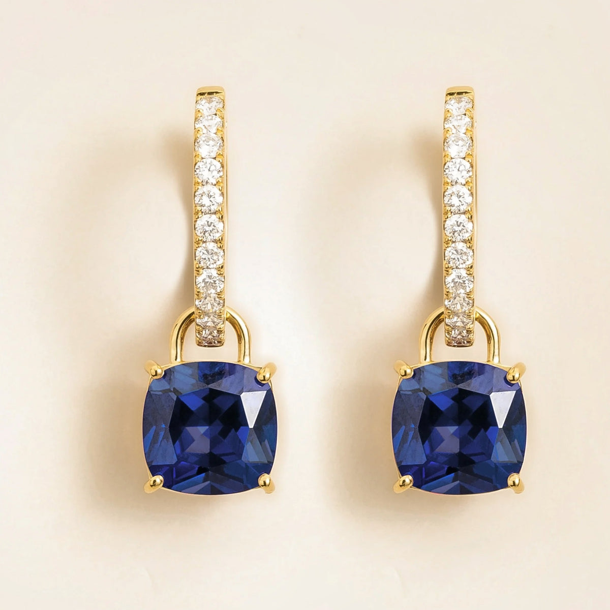 A pair of Roue drop earrings in gold, featuring blue sapphires and diamonds, with a cushion cut design.