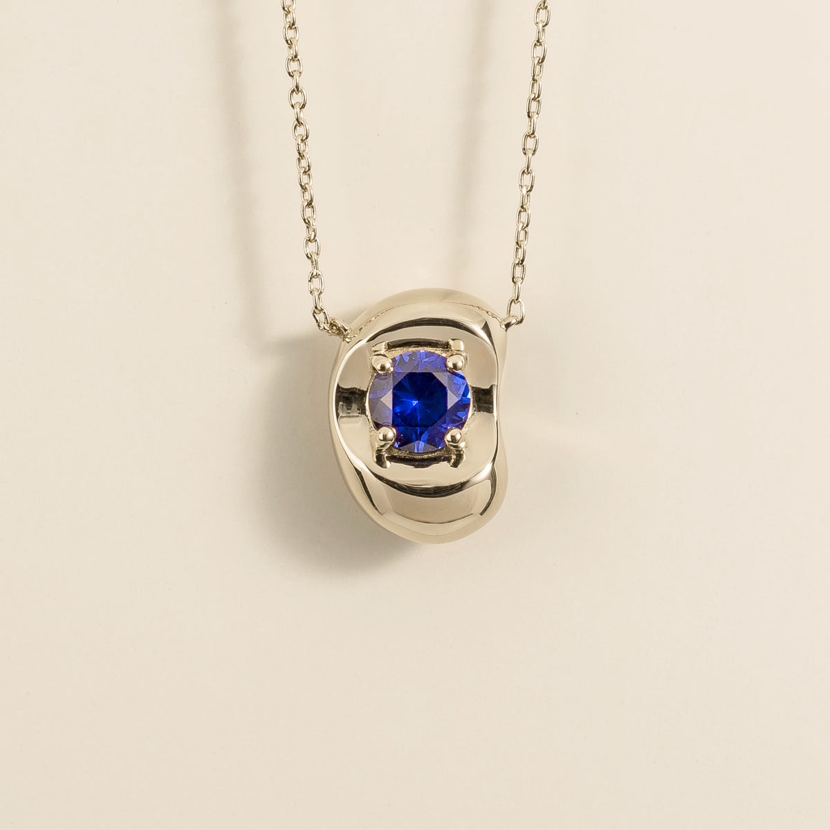 Fava round lab-grown blue sapphire pendant necklace in white gold, sculpted pebble setting, front view | Juvetti London