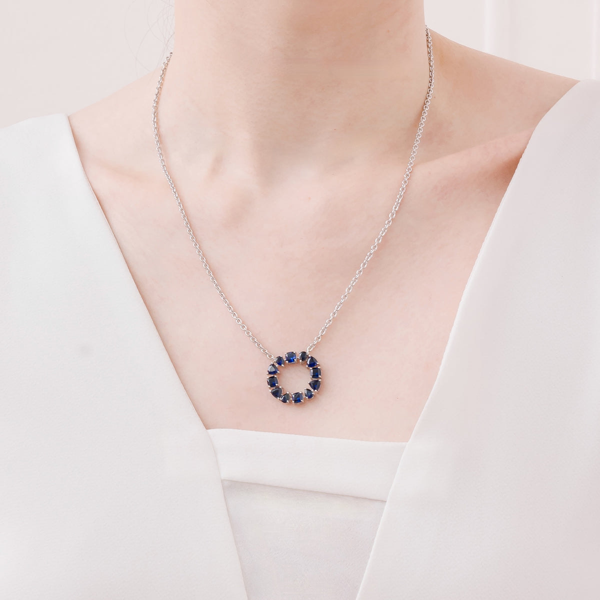 Glorie blue sapphire open circle pendant necklace in white gold, mixed-cut lab-grown sapphires, worn by a model | Juvetti London