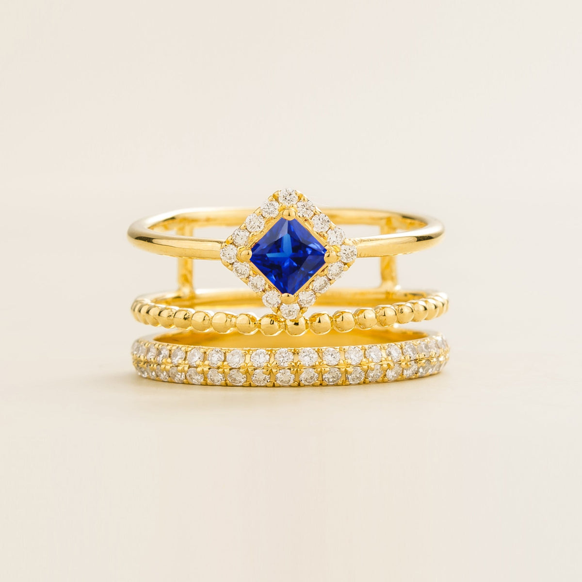 Amici triple-band stacking ring in gold, princess-cut lab-grown blue sapphire in a diamond halo with beaded and pavé bands, front view | Juvetti London