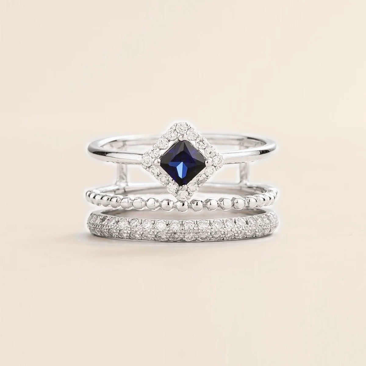 Amici triple-band stacking ring in white gold, princess-cut lab-grown blue sapphire in a diamond halo with beaded and pavé bands, front view | Juvetti London