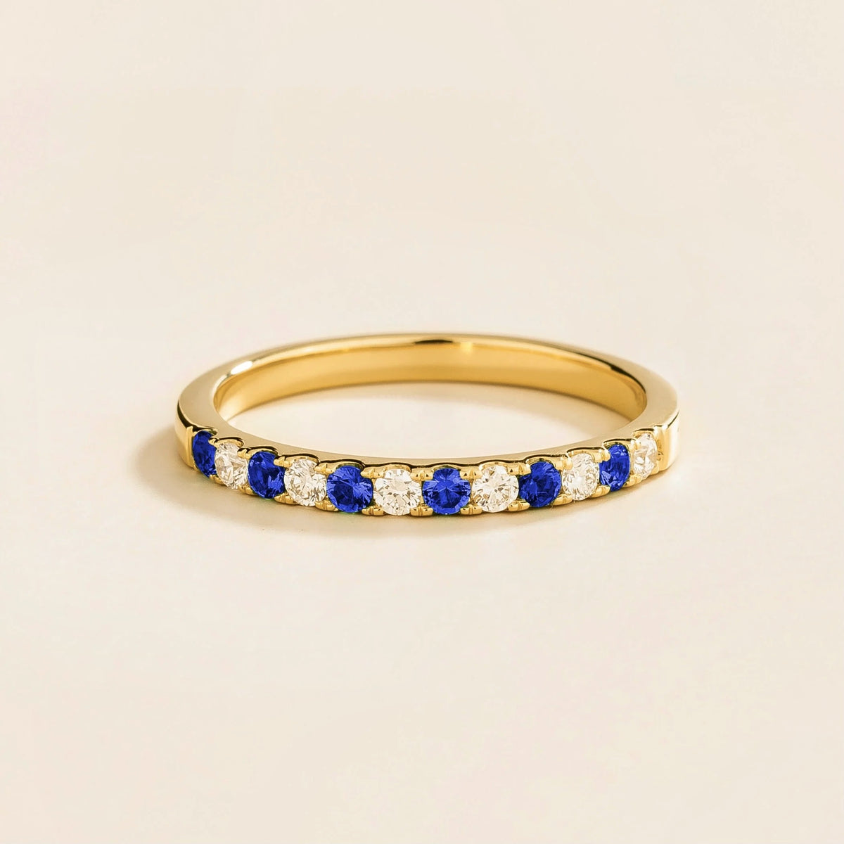 Half eternity gold ring with alternating blue sapphire and diamond elements along its circumference.