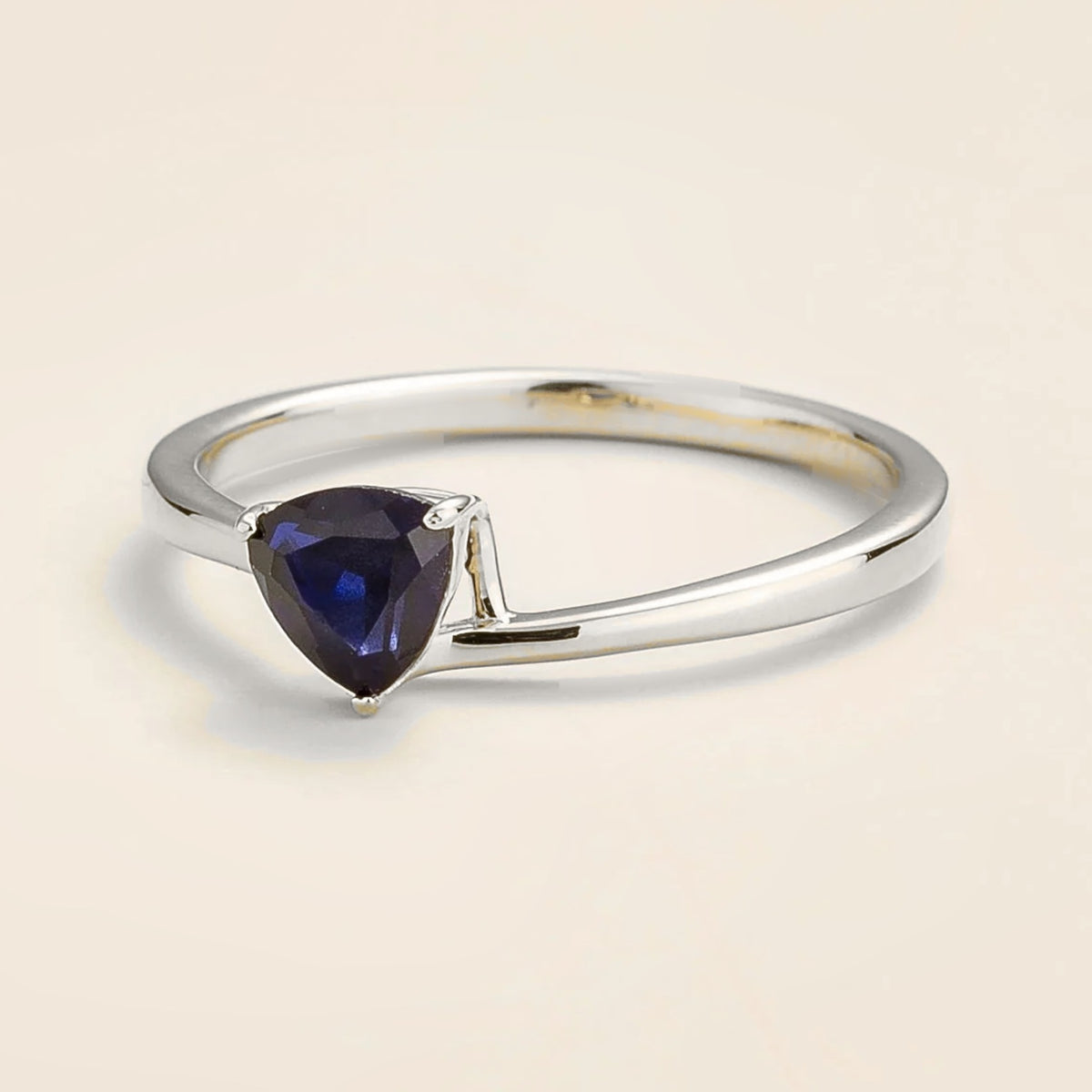 Trillion Blue Sapphire Solitaire Ring in White Gold against beige background