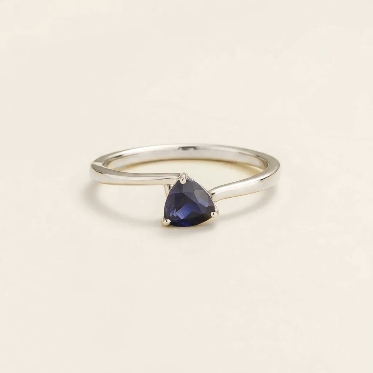A solitaire white gold ring with a trillion-cut blue sapphire in a curved modern setting on a plain background.