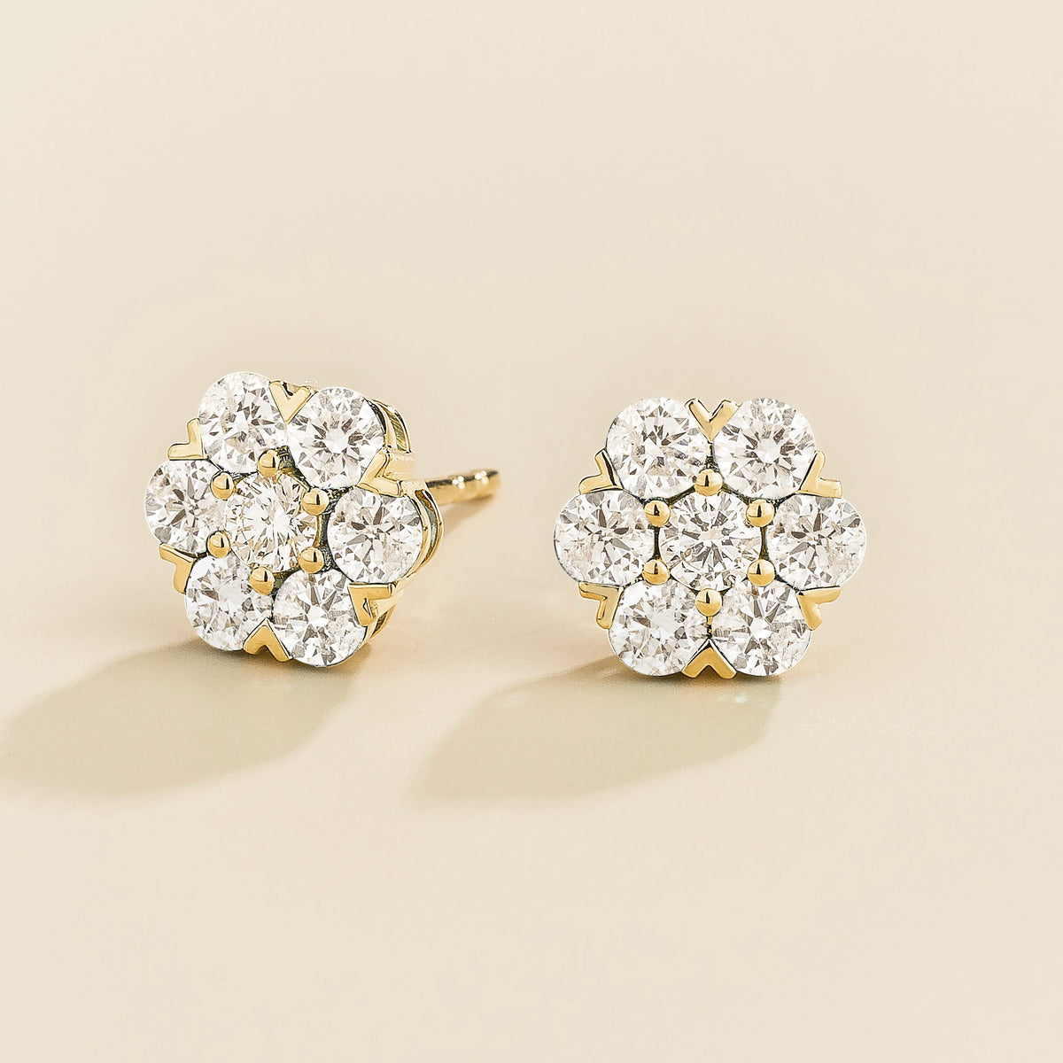 Gold earrings with diamond gemstones in flower shape on a beige background