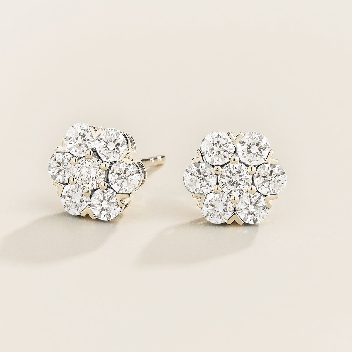 Pair of diamond cluster earrings in flower shape on a light beige background