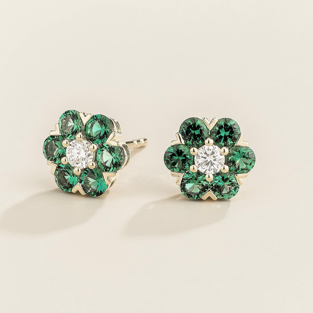 A pair of white gold earrings featuring a central diamond with emerald accents arranged in a floral daisy pattern.