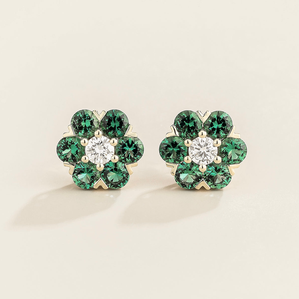 A pair of white gold earrings featuring a central diamond surrounded by five emerald stones, designed in a floral pattern.