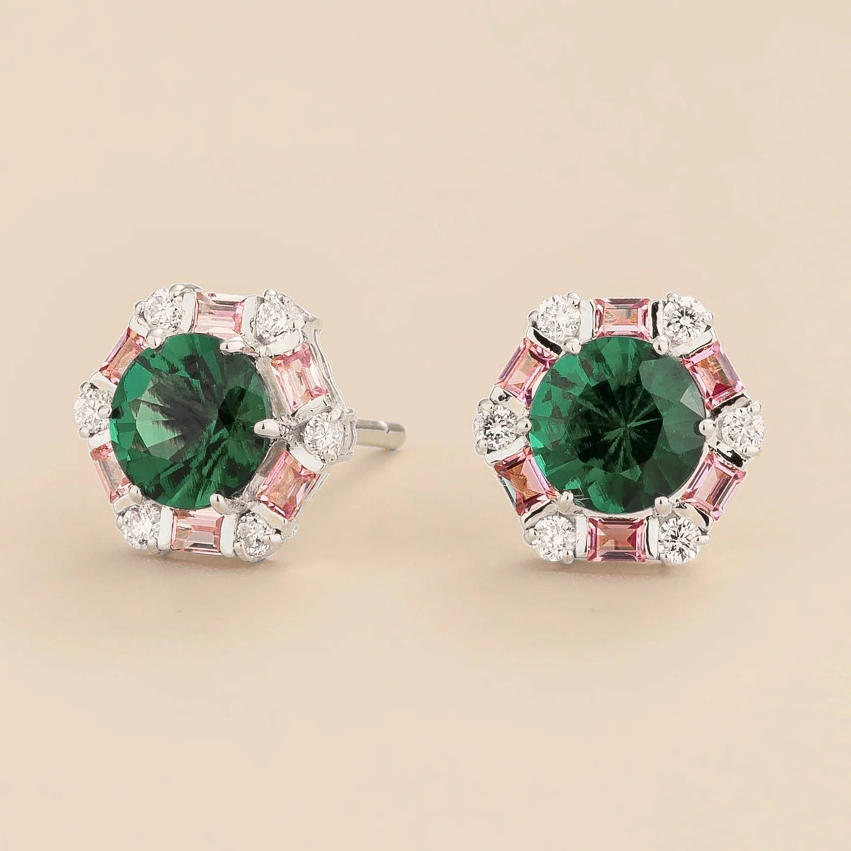 Pair of earrings with green gemstones and pink and white accents on a beige background