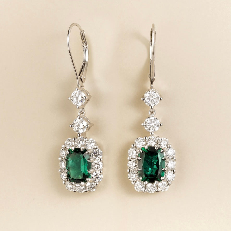 Pippa emerald-cut emerald and diamond halo drop earrings in white gold, lab-grown emeralds hanging from round diamonds on lever-back hooks, angled view
