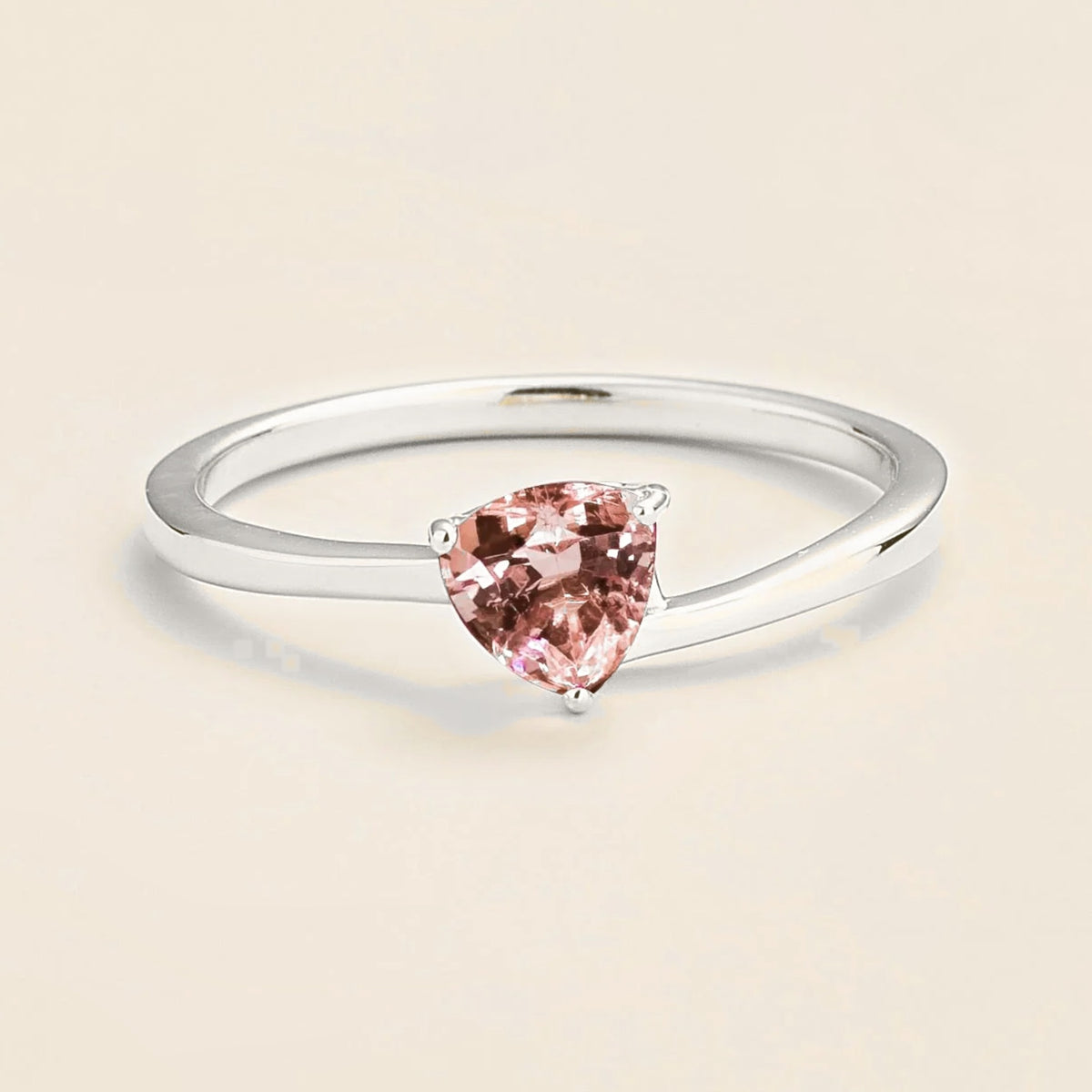 A white gold ring with a trillion-cut morganite centerpiece, set in a modern curved setting on a plain background.
