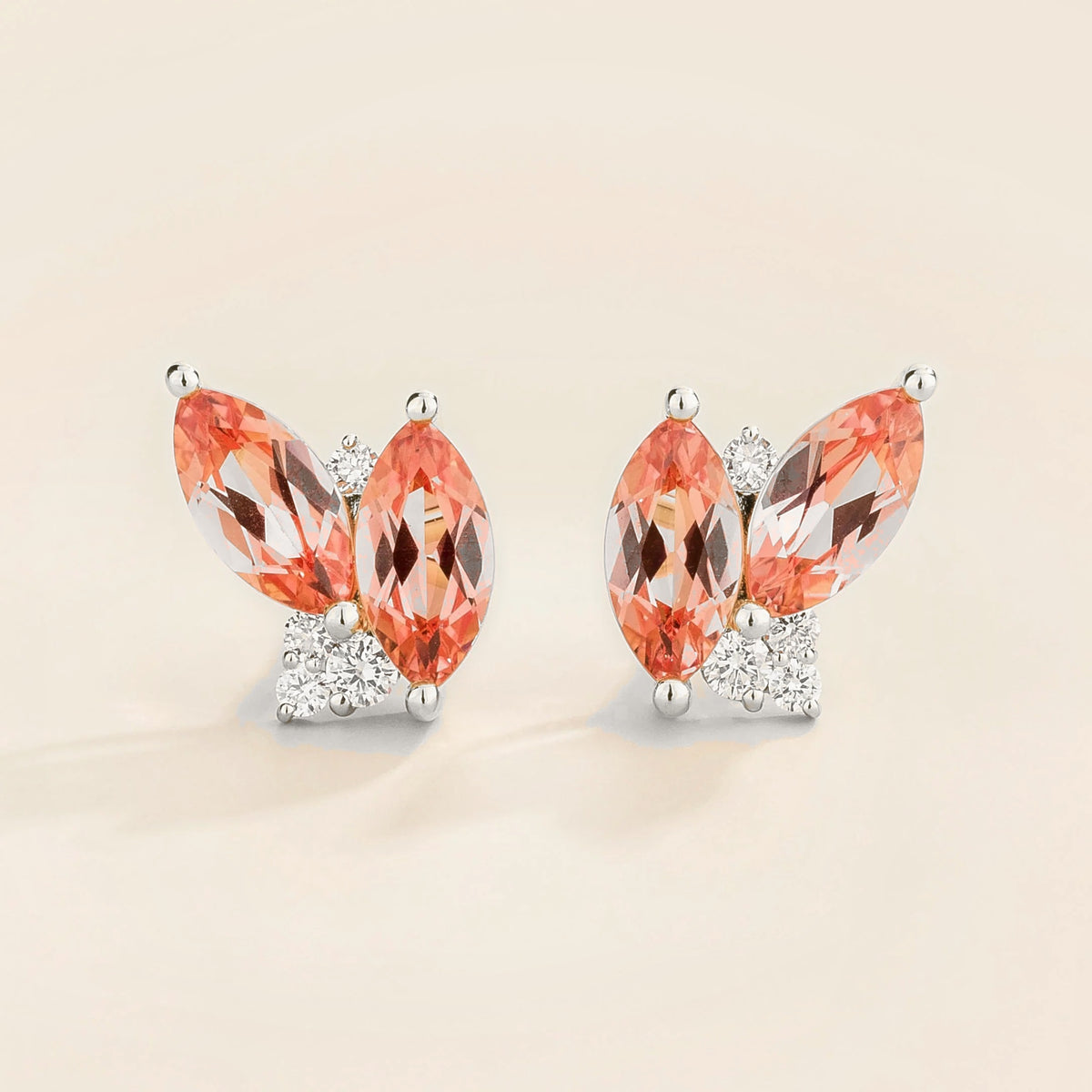 Pair of earrings with marquis padparadscha sapphire gemstones and  white gold with diamond accents on a light background