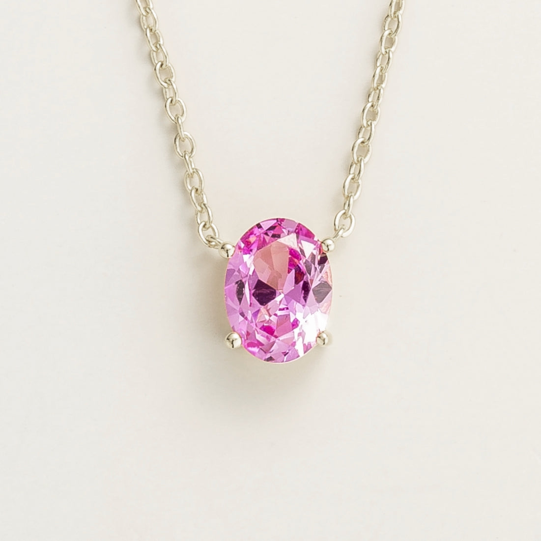 A white gold necklace with oval pink sapphire solitaire pendant on a chain.