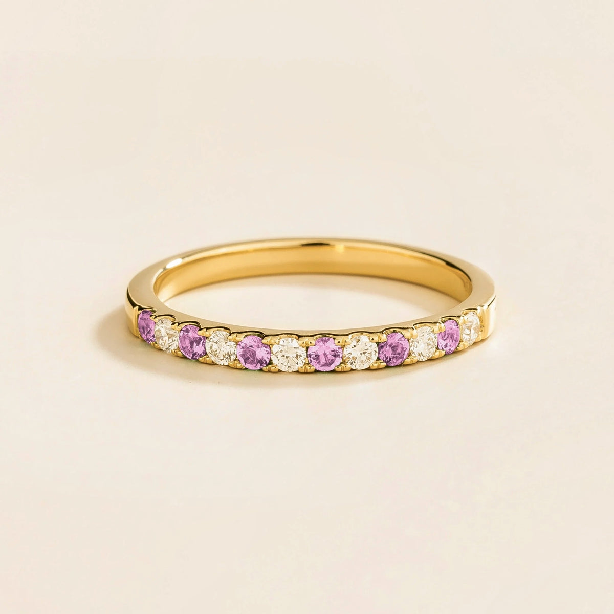 A half eternity gold ring with pastel pink sapphire and diamond accents on a plain background.