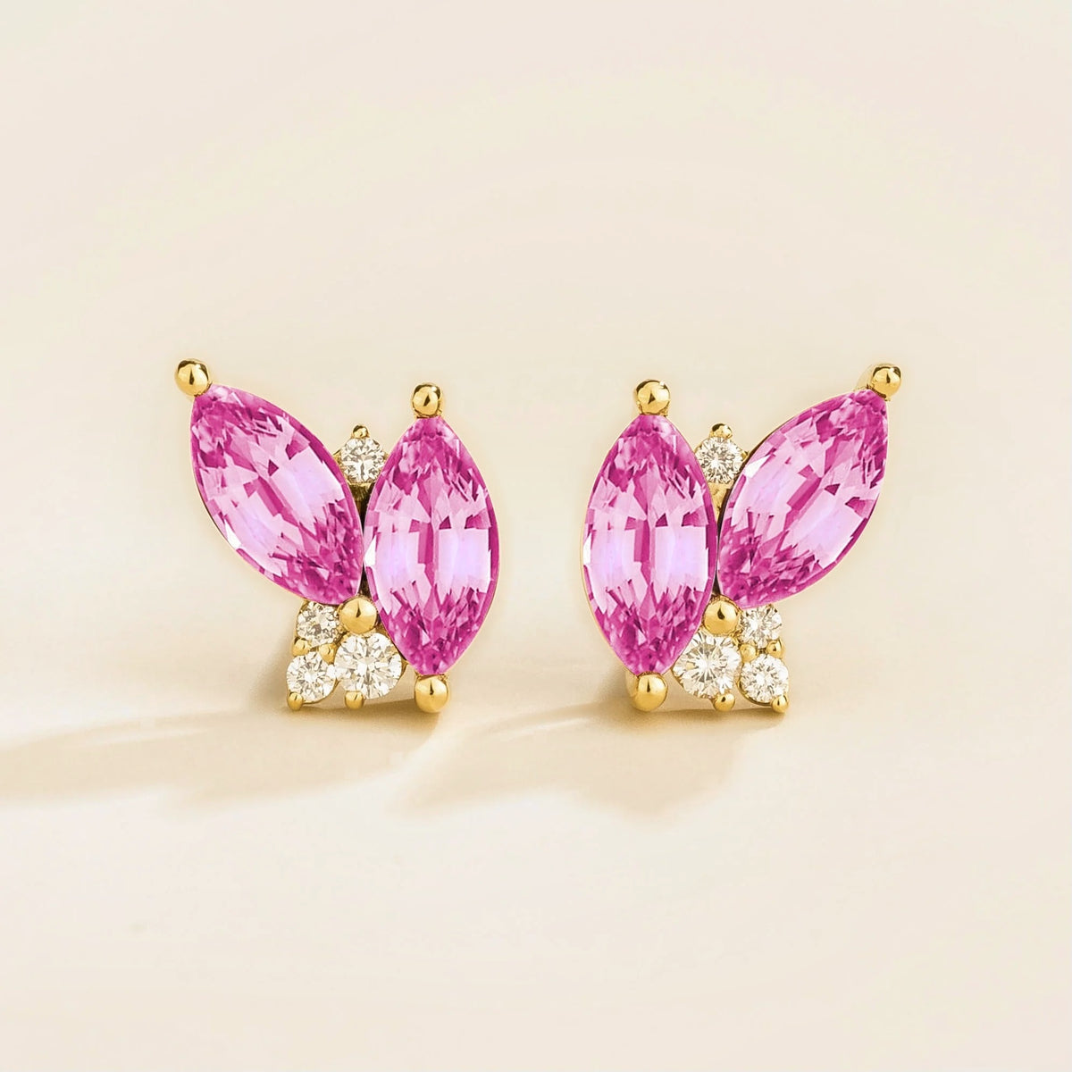 A pair of marquis pink sapphire and round diamond earrings set in gold, with a butterfly-like shape and small round diamonds on the hooks.